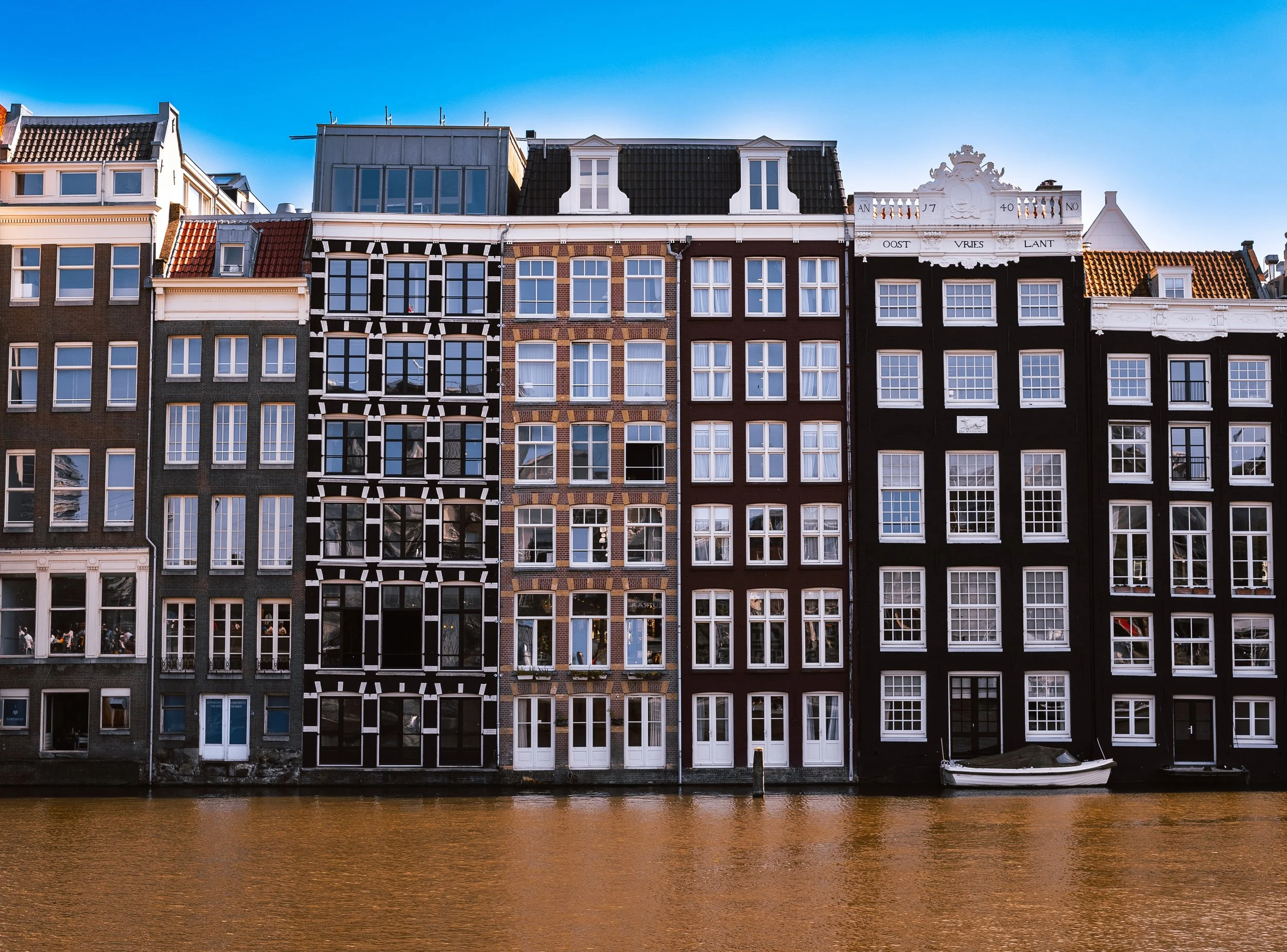 Colorful row of traditional European buildings along a canal with a boat docked in front, under a blue sky.