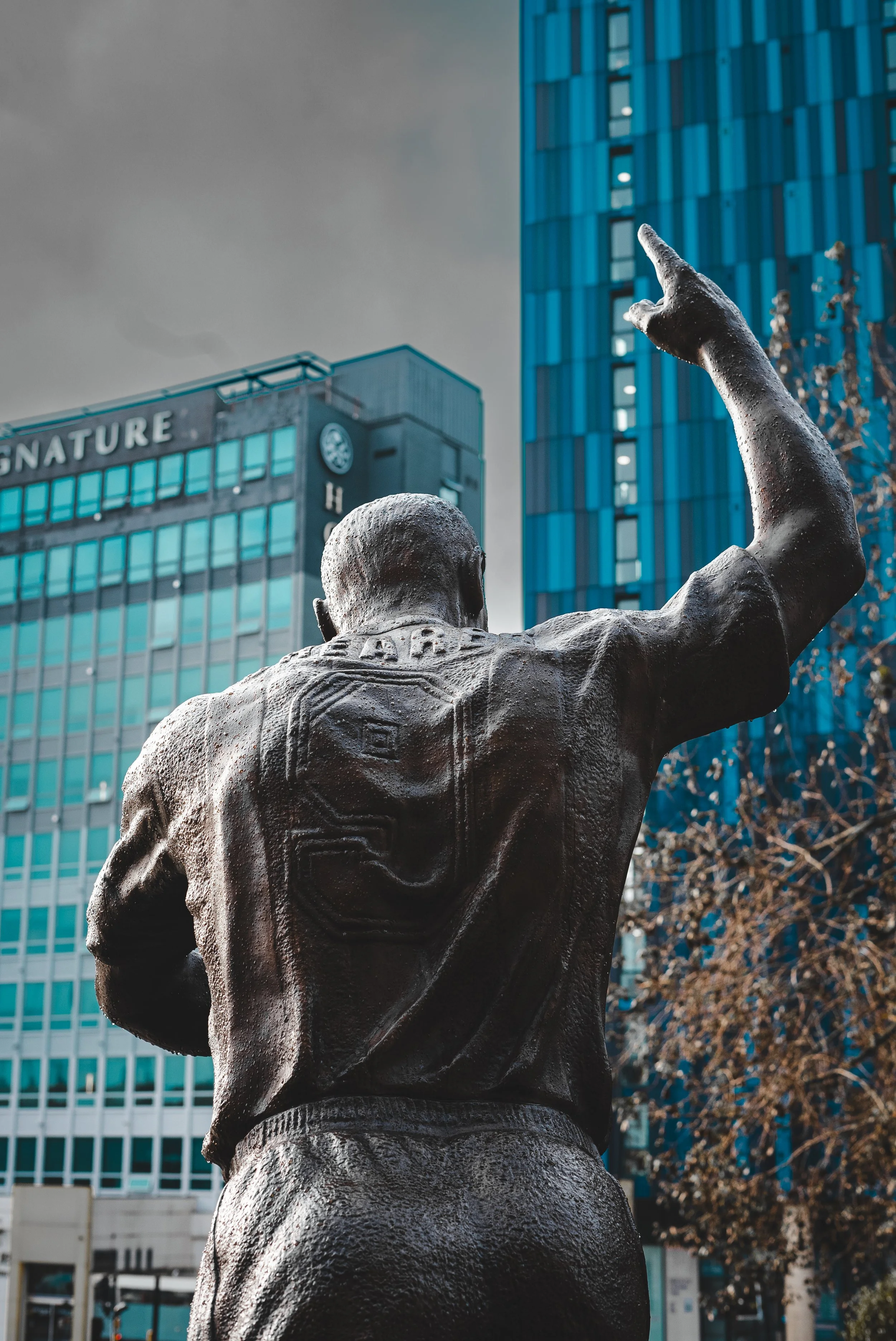 Bronze statue of a man with his arm raised, outdoors in front of modern glass buildings.