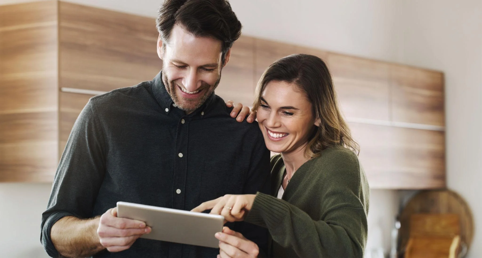 A happy man and woman looking at a tablet together in a cozy indoor setting.