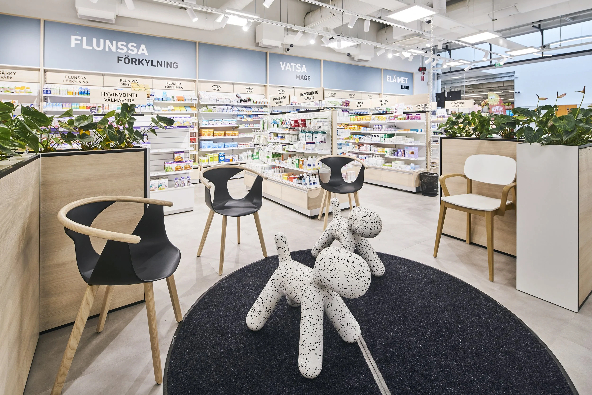Tämä on kuvitus apteekkiin, jossa on hyllyjä lääkkeillä ja terveyspuheilla. Kuvassa on myös istuimia ja sisäpiha, jonka ikkunasta näkyy ulos.