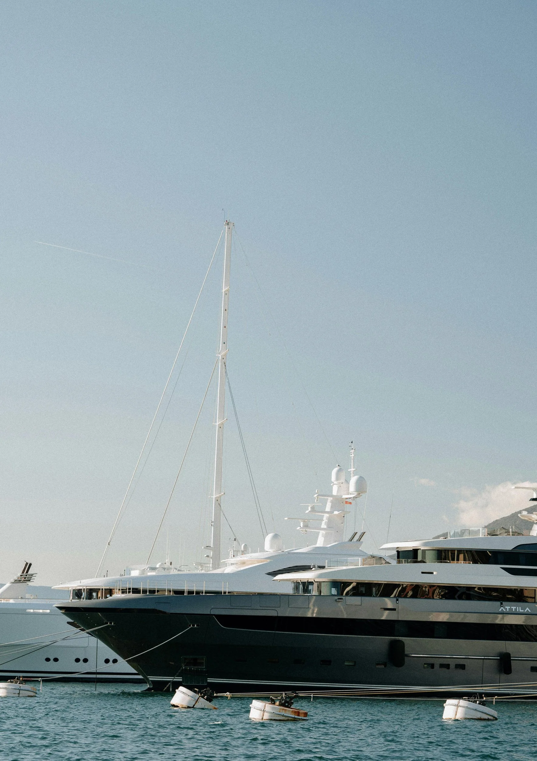A large luxury yacht docked in a marina with several smaller boats floating in the water nearby, and a clear sky overhead.