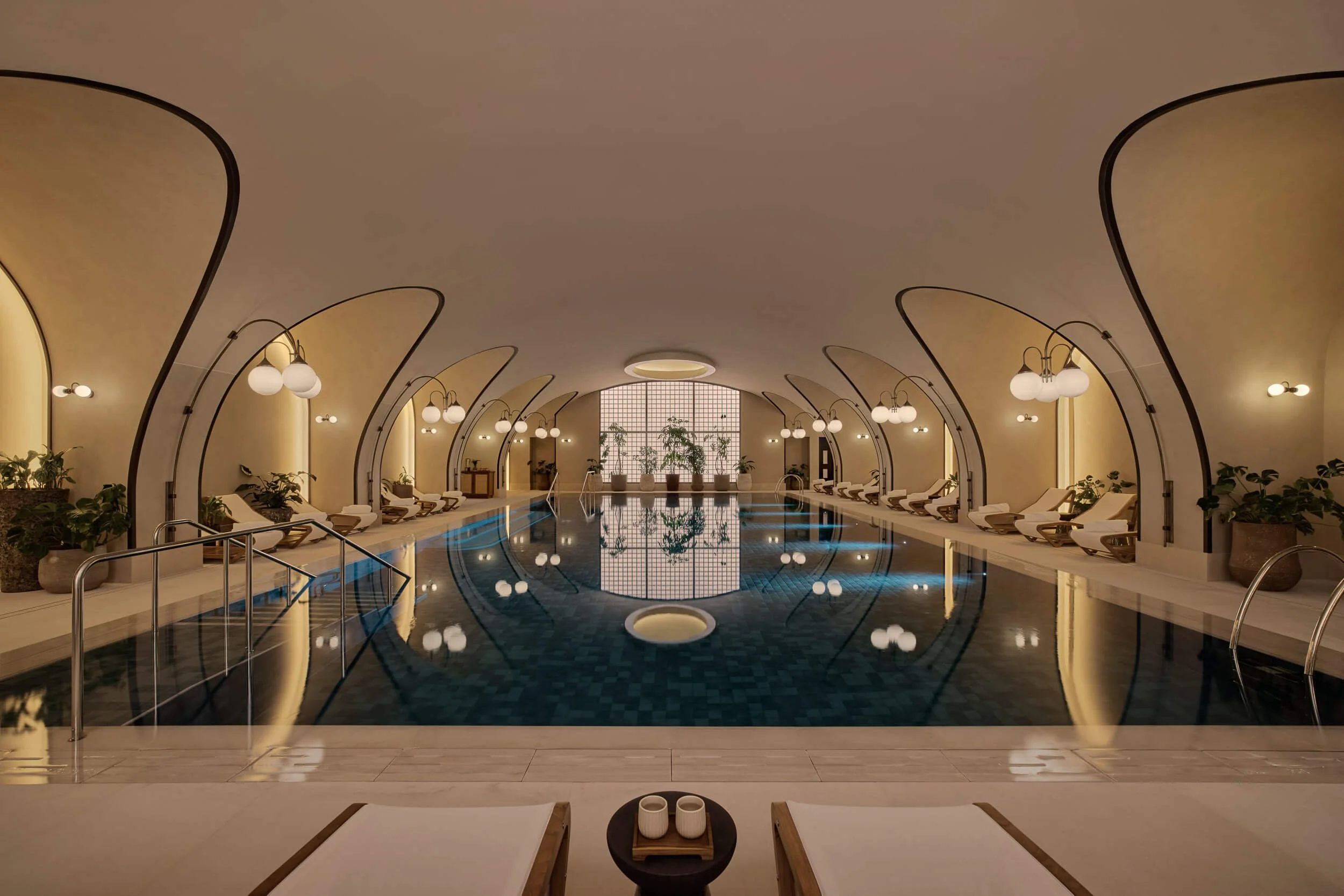 Indoor swimming pool area with lounge chairs, potted plants, and elegant lighting fixtures in a warm-toned ambiance.