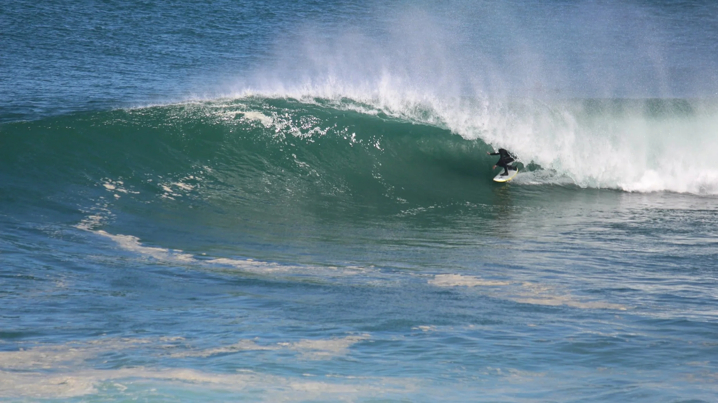 Surfer riding inside a large ocean wave during daytime.