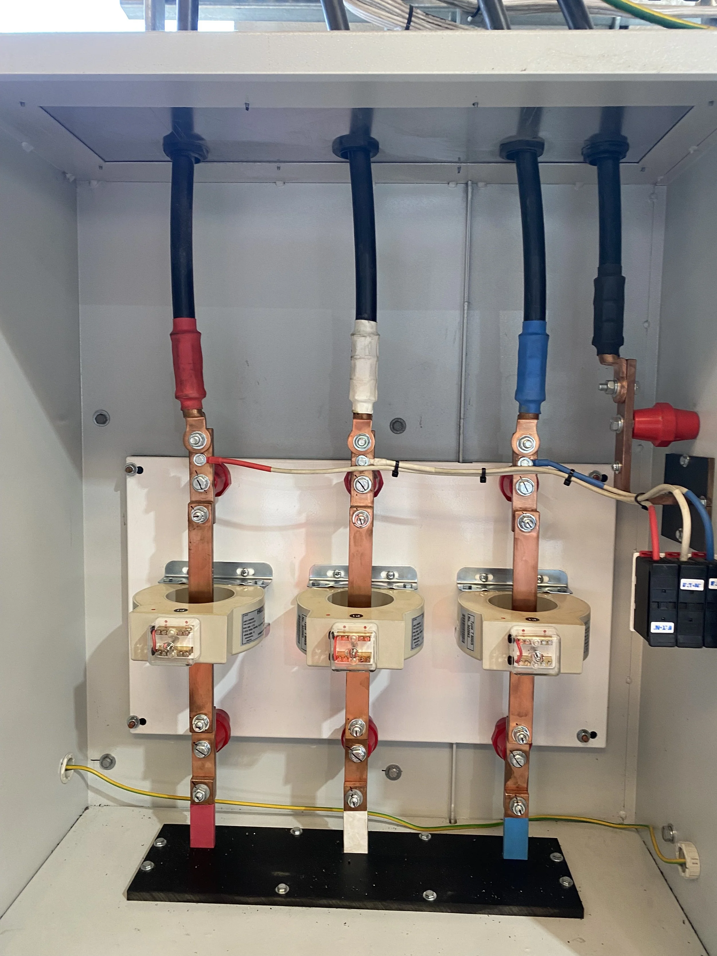 An electrical panel with three large circuit breakers, copper busbars, and colored wires connected to the breakers inside a metal enclosure.