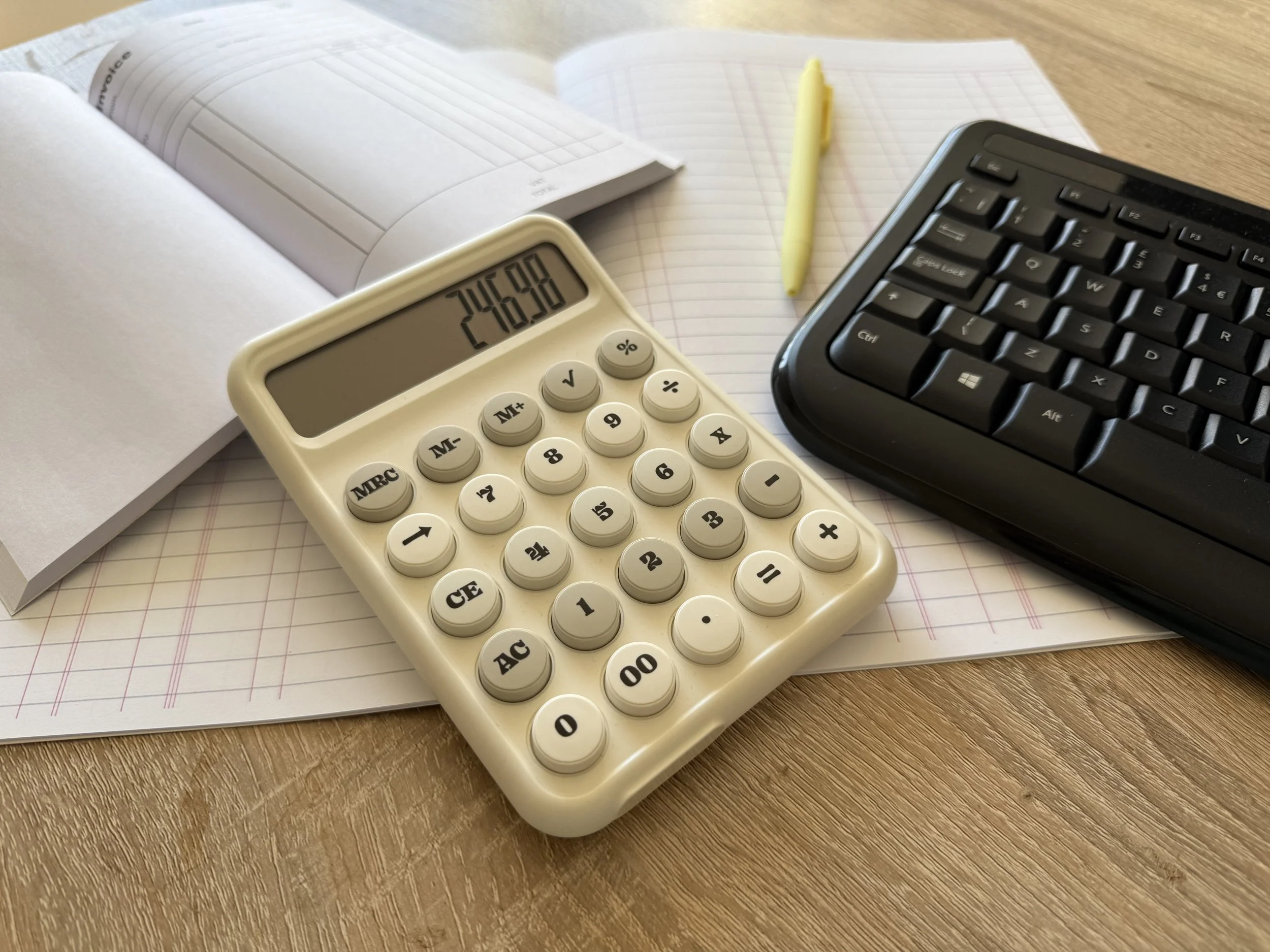 Open notebook, yellow pen, calculator, keyboard on wooden desk.