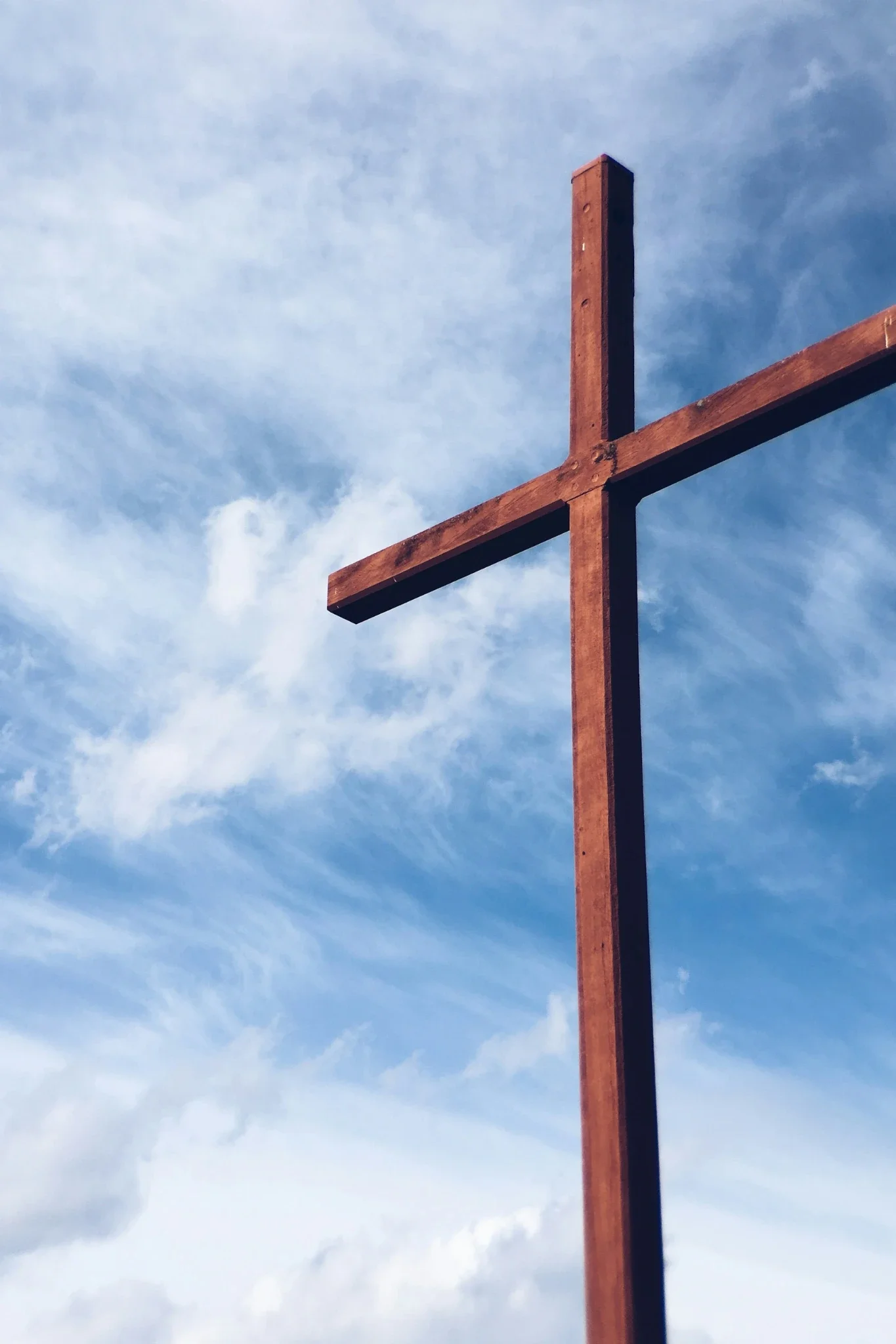 A tall wooden cross standing vertically against a cloudy blue sky.