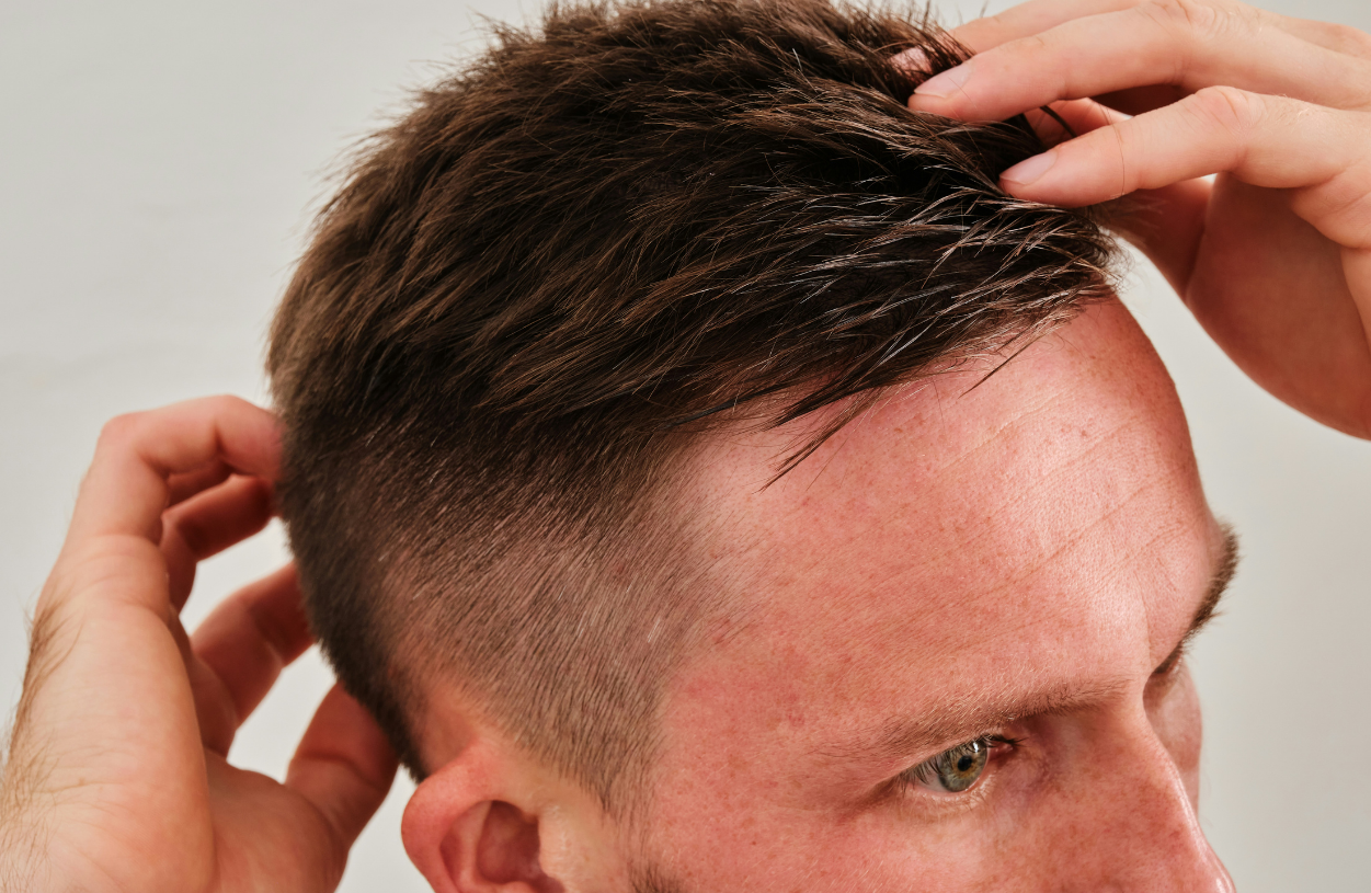 A man with short, styled hair, running his fingers through his hair and touching their head.