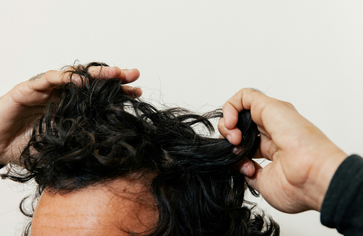 Person with dark curly hair adjusting their hair with both hands.