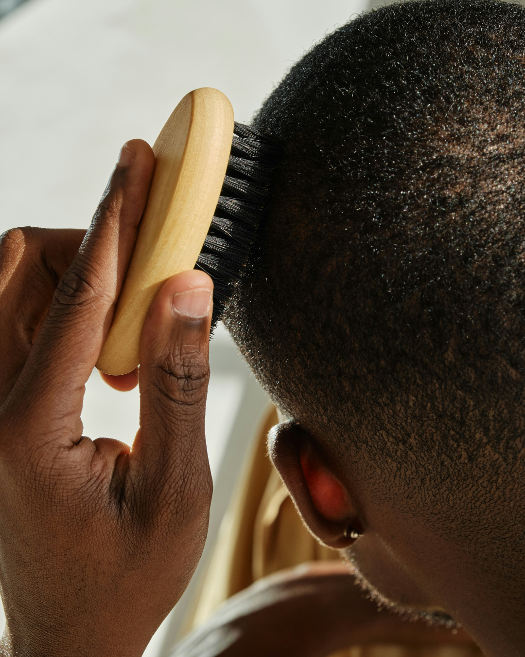 A person combing their short, curly black hair with a wooden hairbrush.