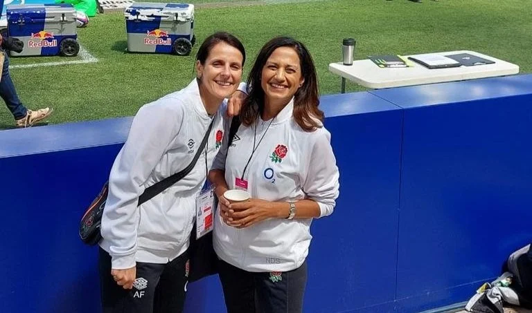 Two women wearing England rugby jackets at an outdoor event