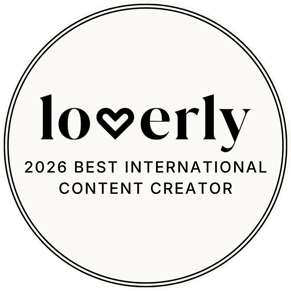 A circular badge with a black outline. Inside, the word 'lovely' is written in large black font, with a heart shape replacing the letter 'v'. Below, it says '2026 Best International Content Creator.'