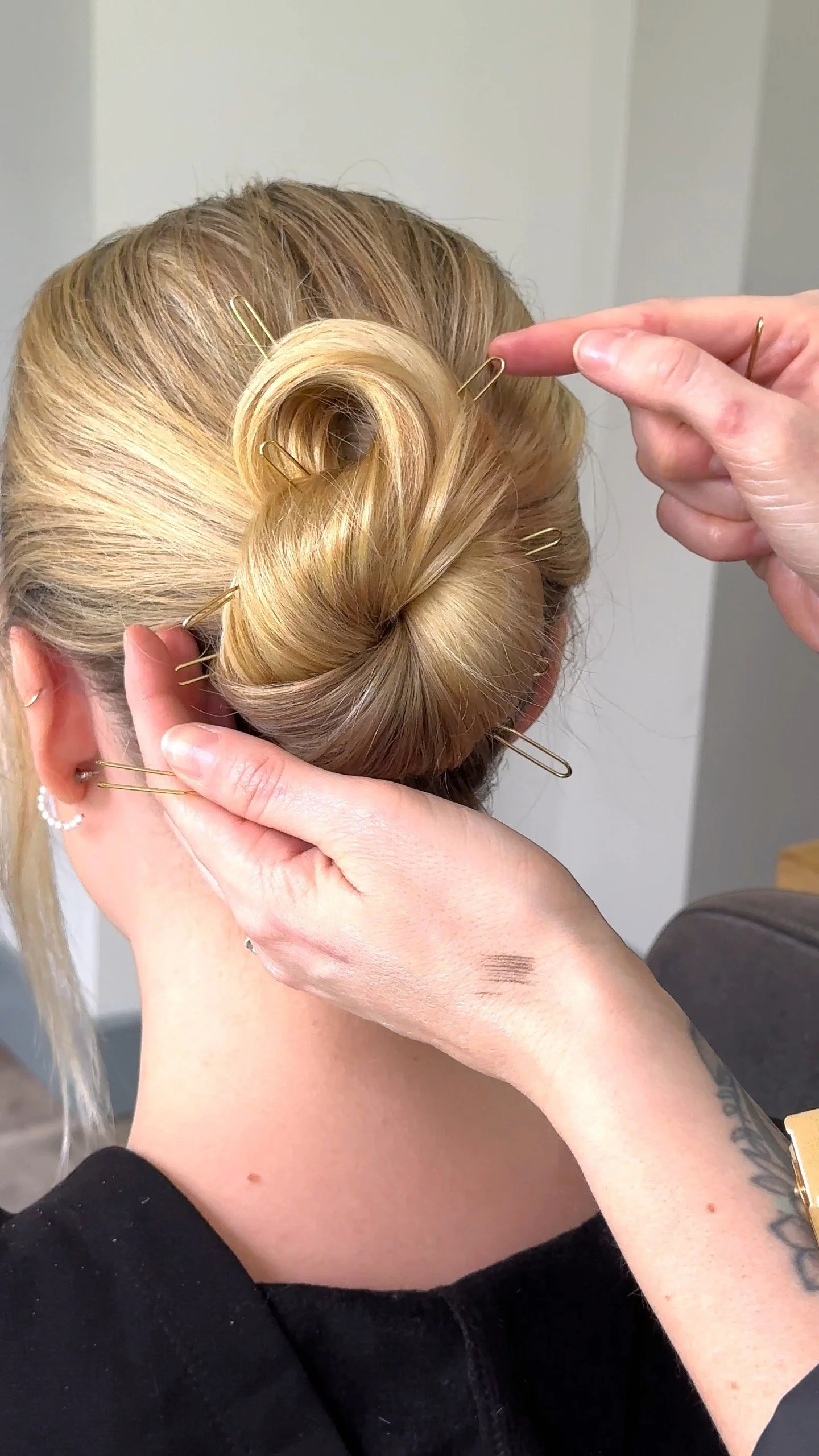A person styling a woman's blonde hair into a bun using multiple hairpins.