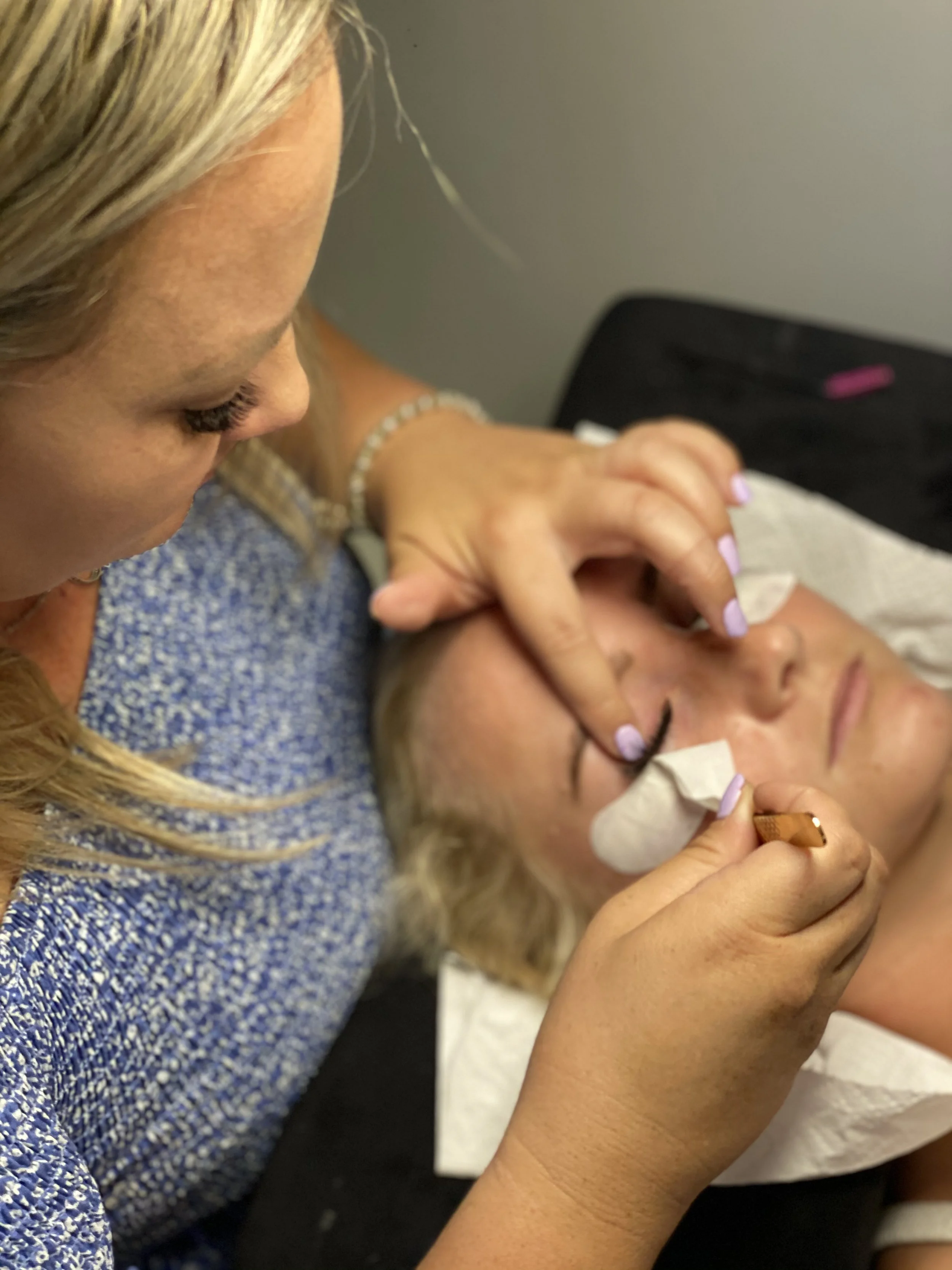 A woman receiving eyelash extensions or eyelash care from a beautician at a beauty salon.