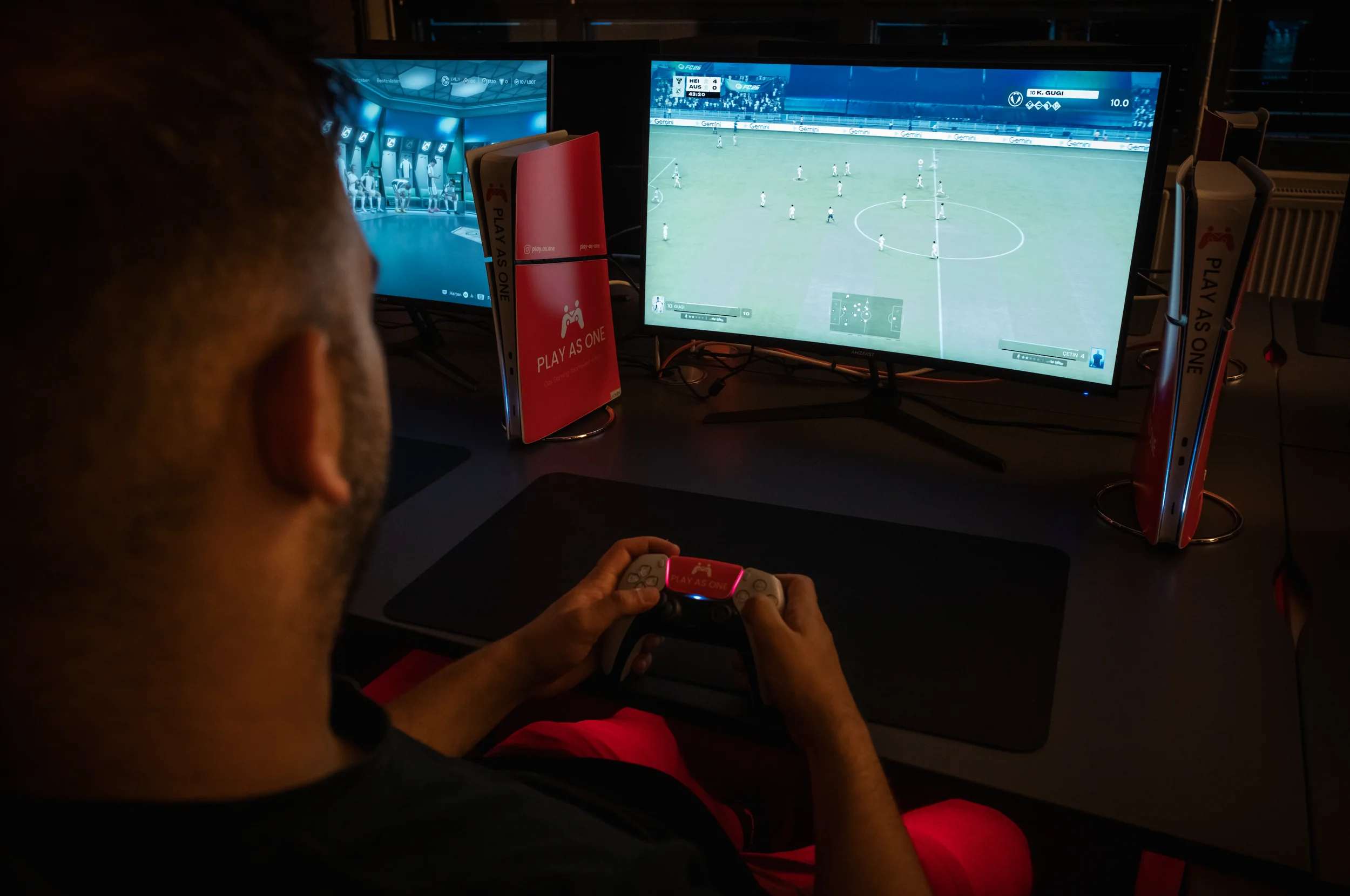 Jemand spielt ein Fußball-Videospiel auf einem Controller, während er vor zwei Computermonitoren sitzt. Auf dem rechten Bildschirm ist eine Fußballspielszene zu sehen, auf dem linken Bildschirm sind Menüs und Einstellungen sichtbar.