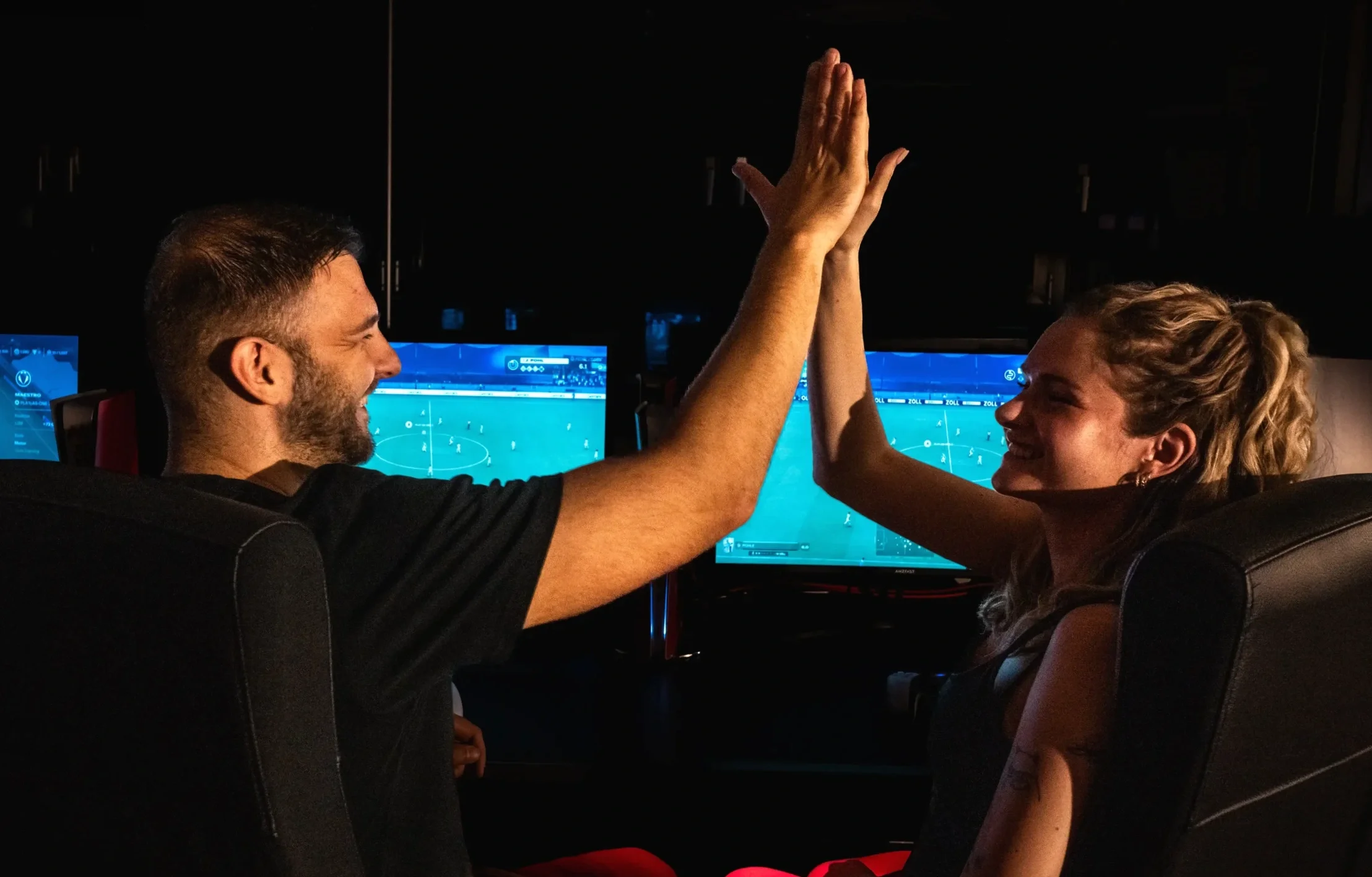 Ein Mann und eine Frau, die in einem dunklen Raum vor Computerbildschirmen sitzen, geben sich die High Five.