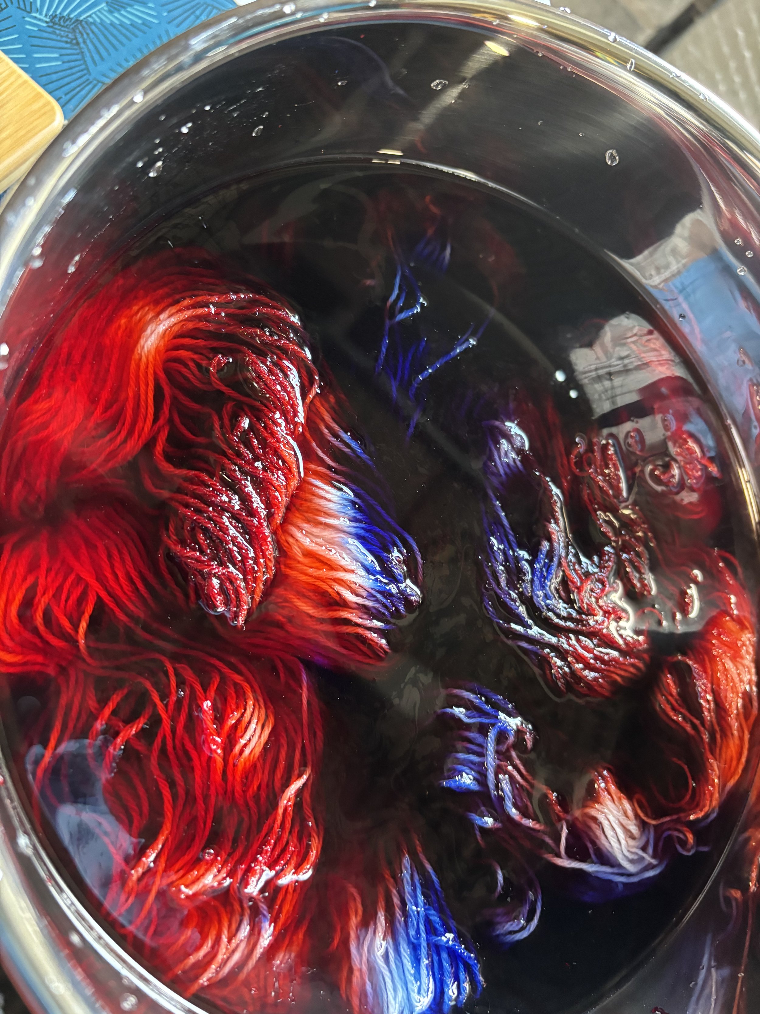Close-up of a glass of swirling red, blue, and white dye in water, creating colorful patterns.