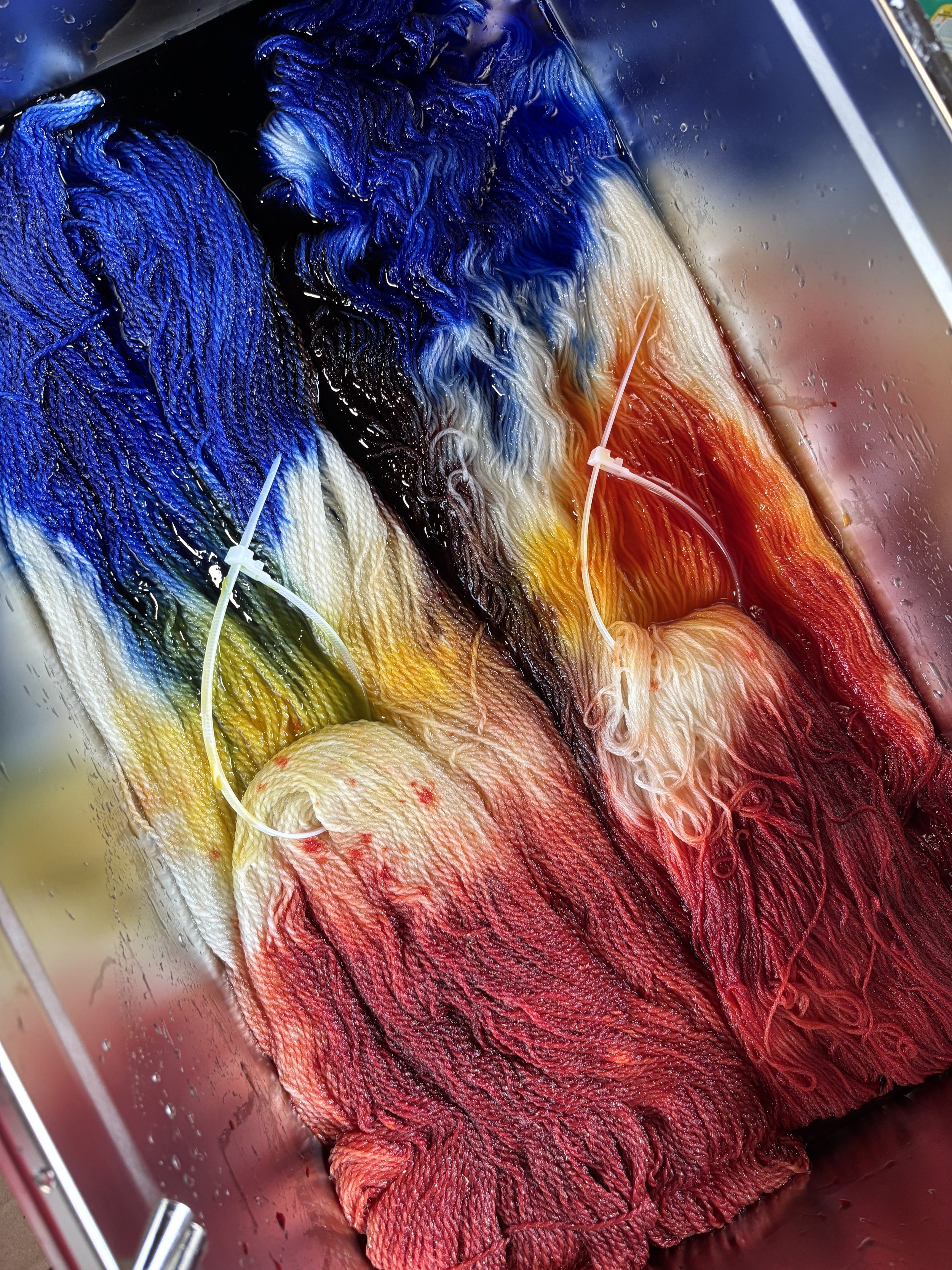 Colorful dyes on fabric in a dyeing process, with various shades of blue, black, yellow, red, and orange.