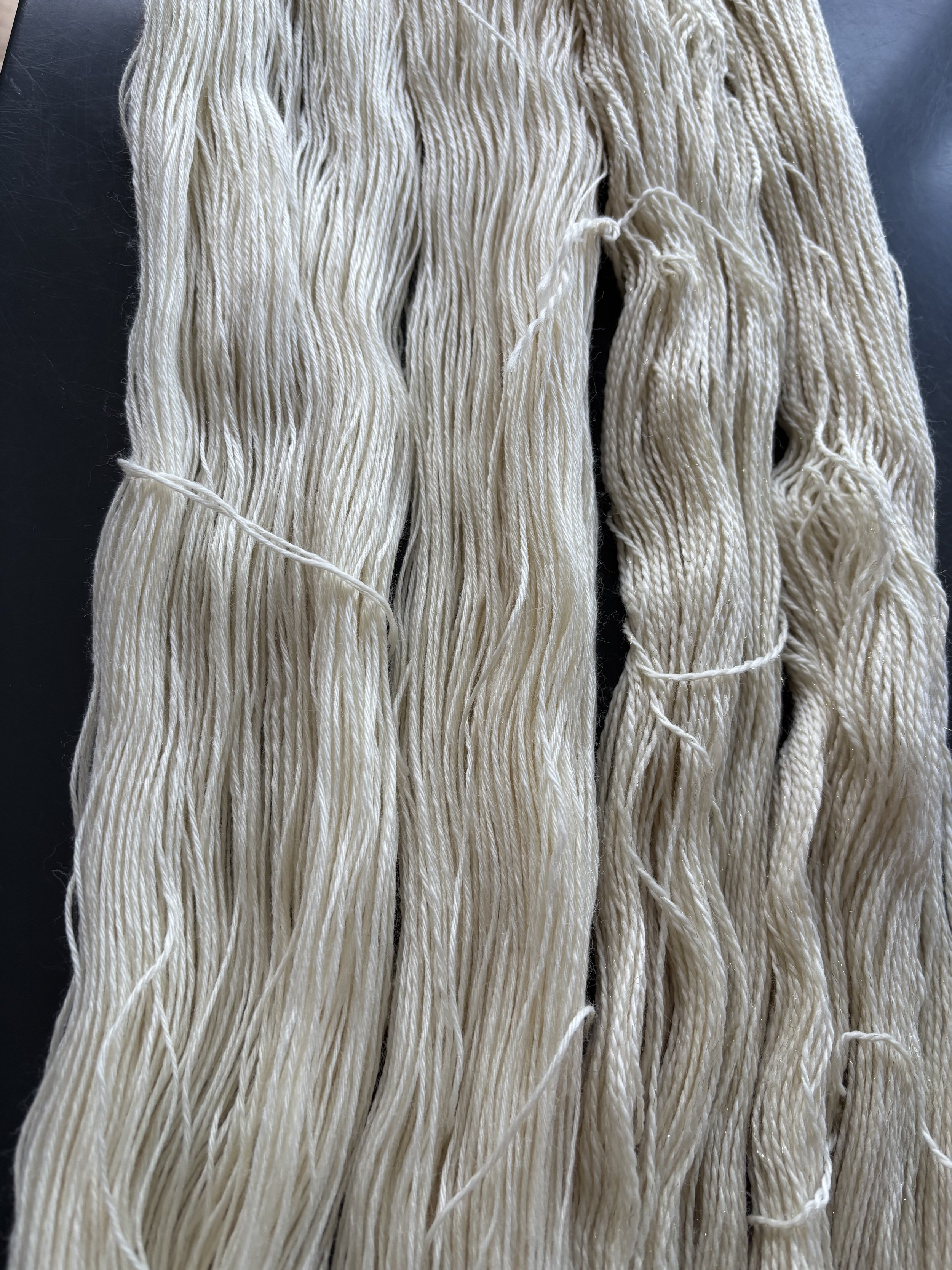 Several bundles of cream-colored yarn or string, loosely arranged on a dark surface.