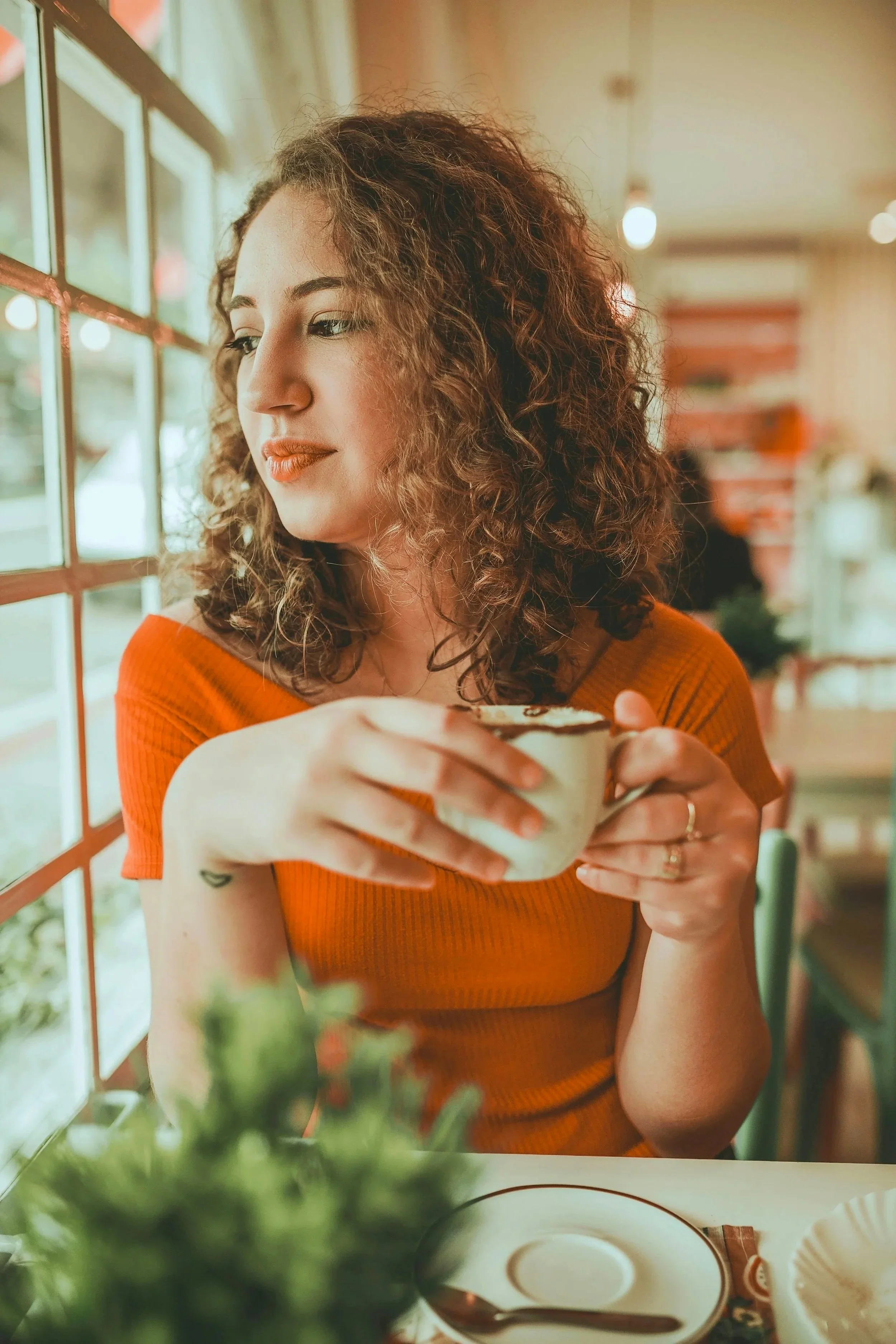 Photo of woman with curly hair looking out the window at a cafe