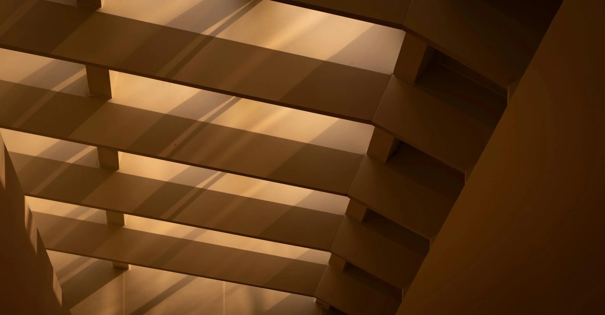Multiple open wooden shelves with shadow patterns cast by window blinds or slats.