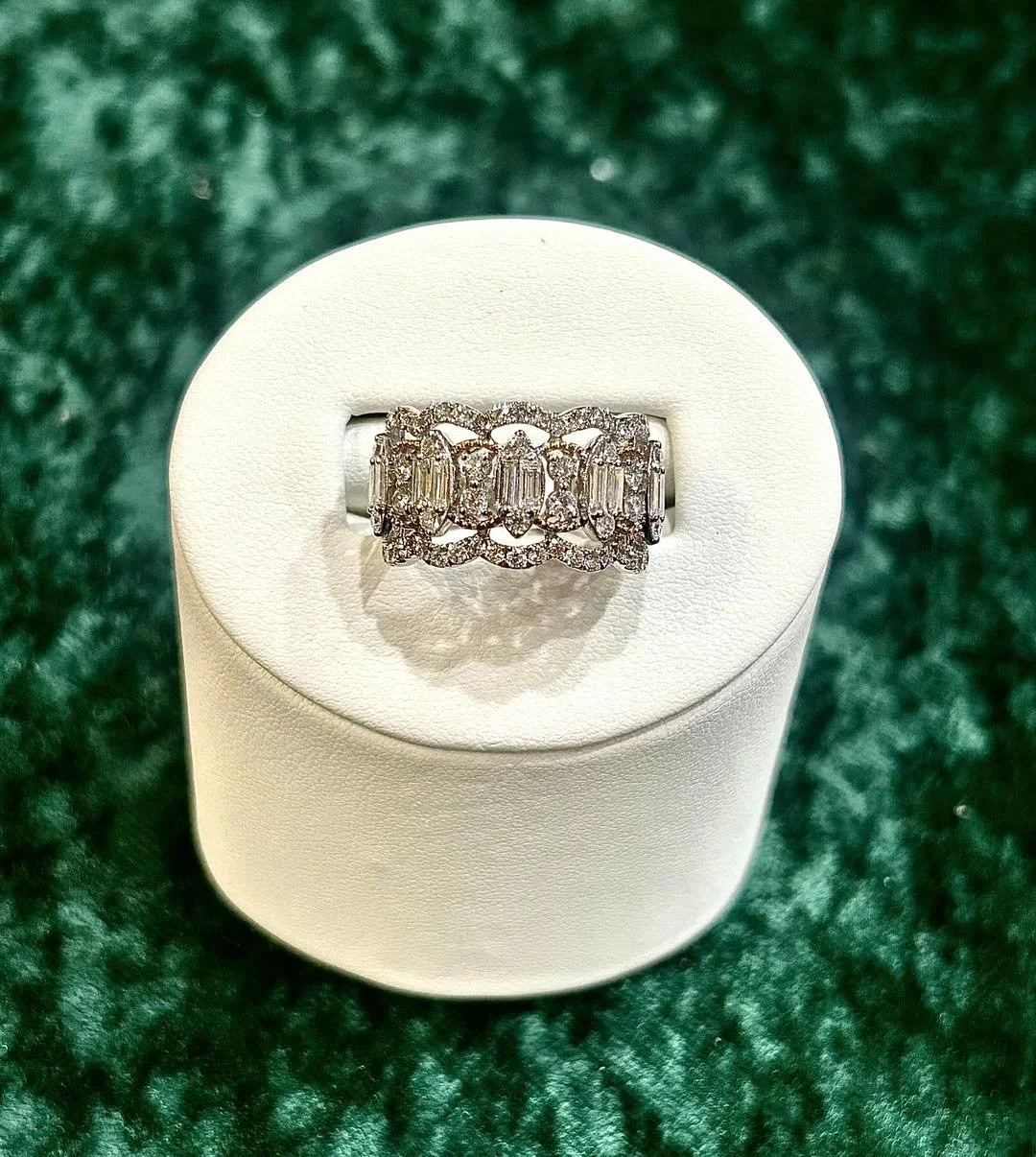 A silver ring with rectangular baguette-cut and round diamonds, displayed on a white ring holder.