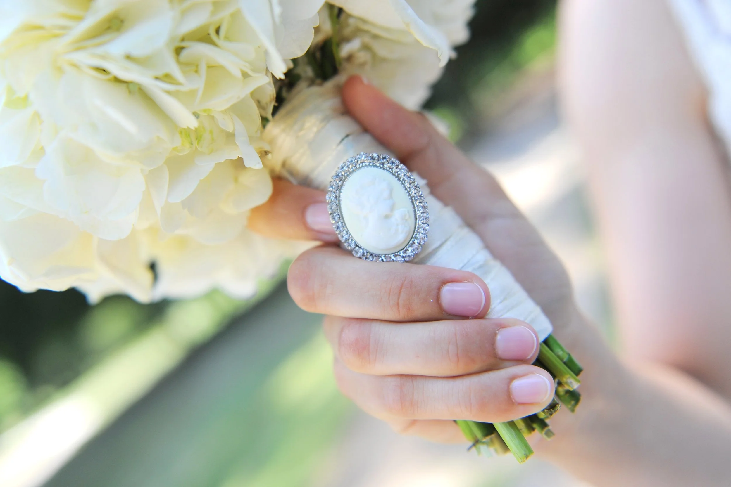 Close-up of a bride's hand holding a bouquet of white flowers, with a large decorative ring on her finger.