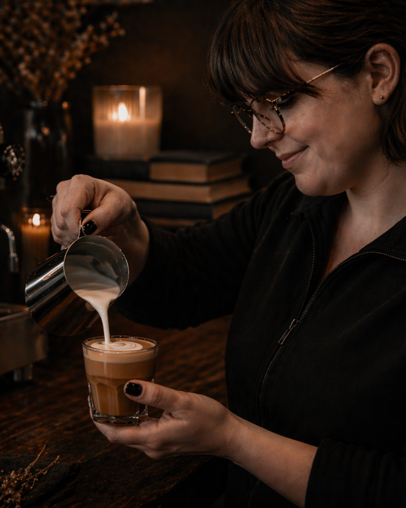 A woman pouring steamed milk into a latte to create latte art.