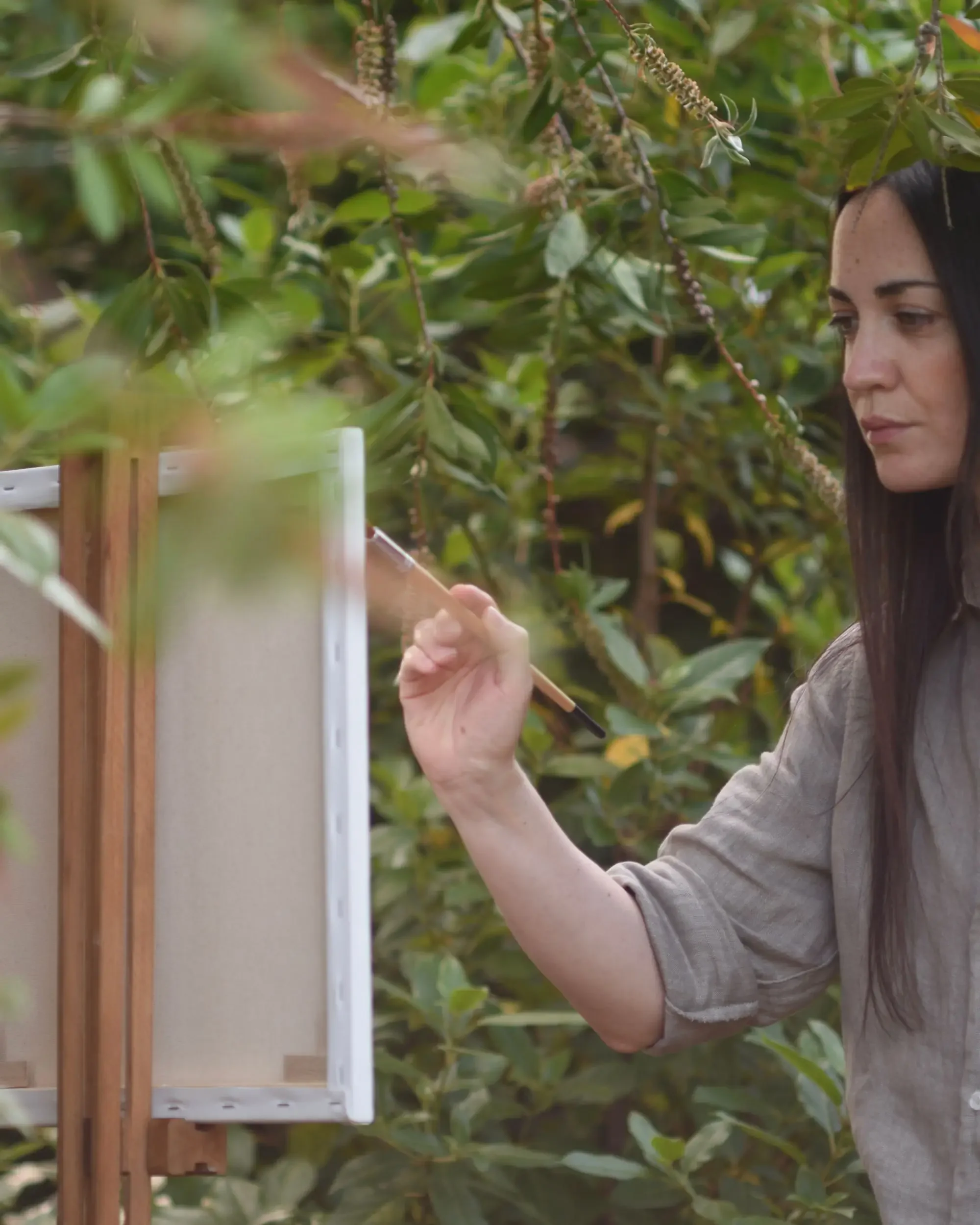 Figurative painter Francesca V Kranz working on a canvas with a paintbrush in her outdoor garden studio in Liguria.