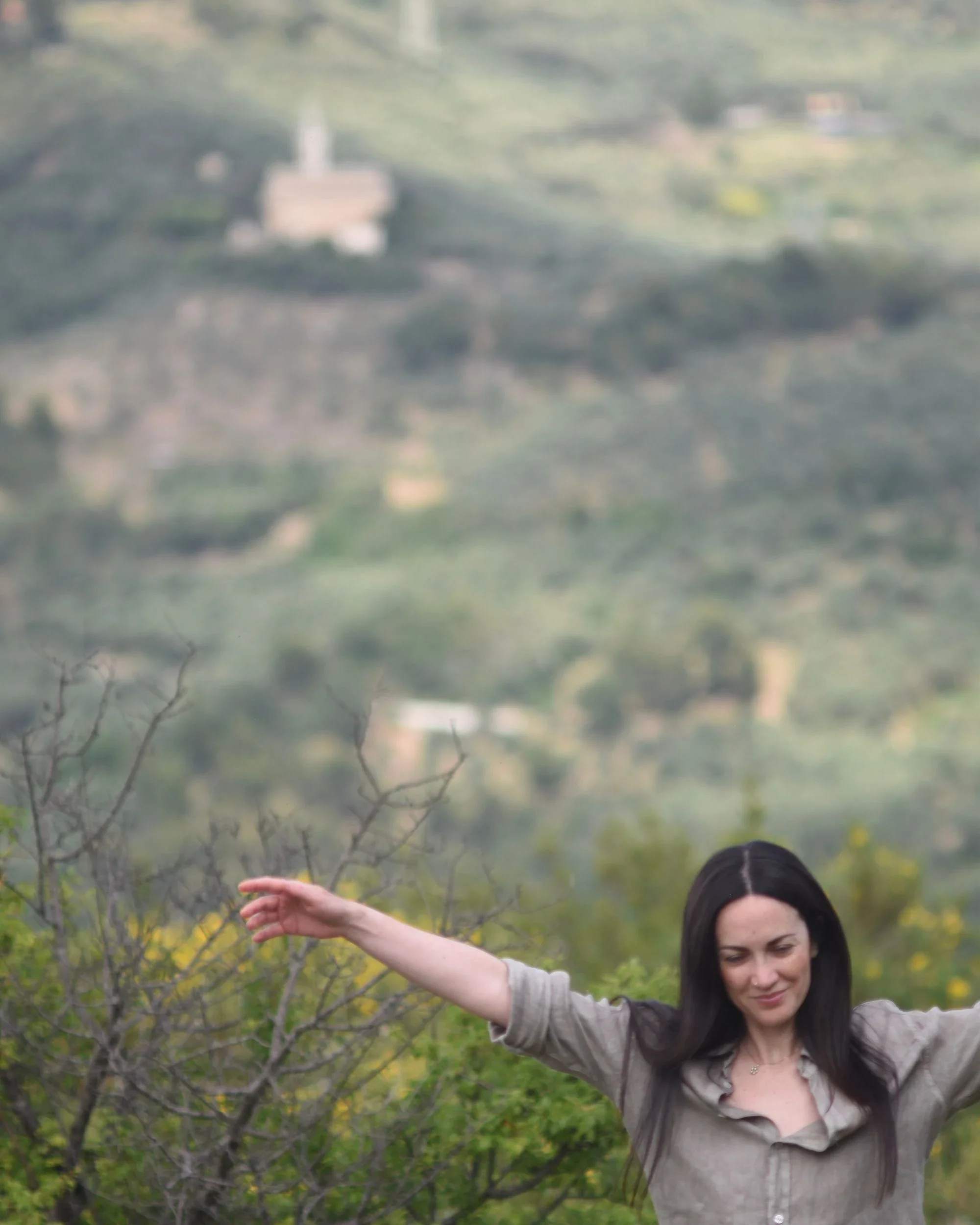 Artist Francesca V Kranz with arms open in the green hills of Liguria, Italy, embodying the philosophy of fine living and intentional existence.