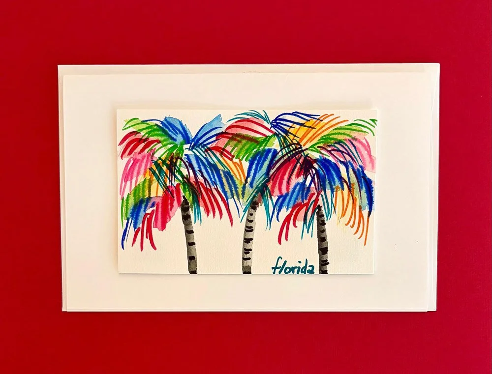 Colorful illustration of three palm trees with multicolored leaves on white paper, with the word "Florida" handwritten at the bottom, placed on a red background.
