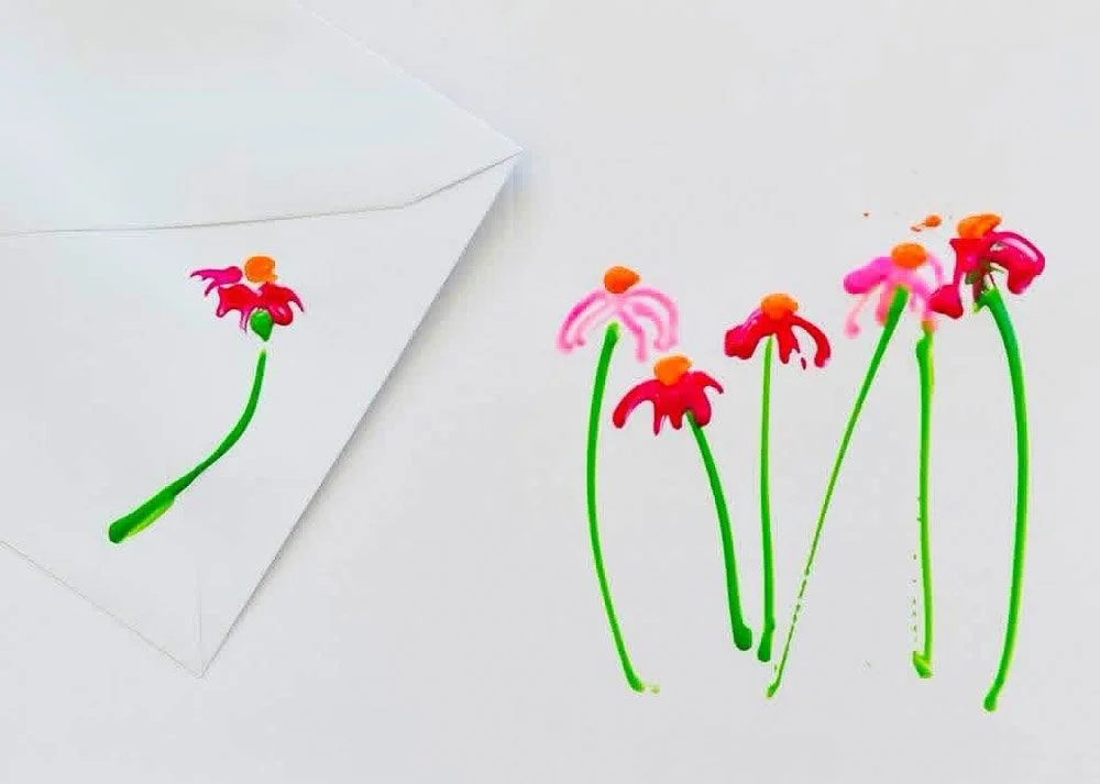 Colorful plastic flowers with green stems and orange centers, some are attached to an envelope, against a plain white background.