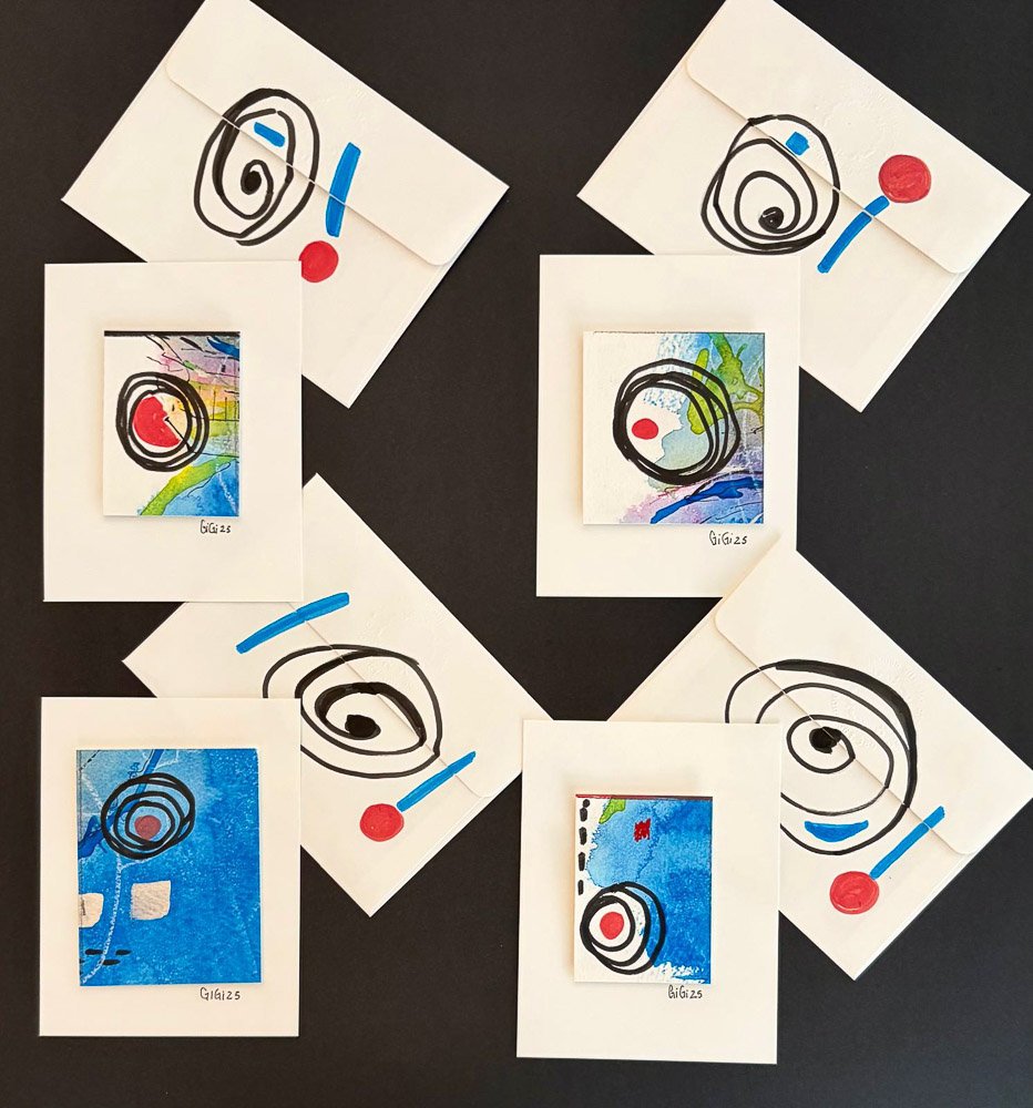 Collection of handmade abstract artworks featuring black spiral lines, red dots, and colorful backgrounds, arranged around white cards with blue highlights on a black surface.