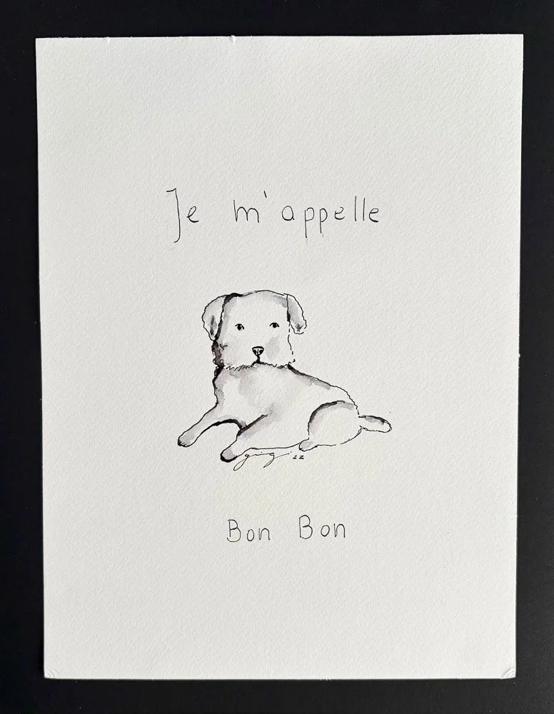 A hand-drawn sketch of a dog with the French phrase 'Je m'appelle' above it, and the English phrase 'Bon Bon' below.