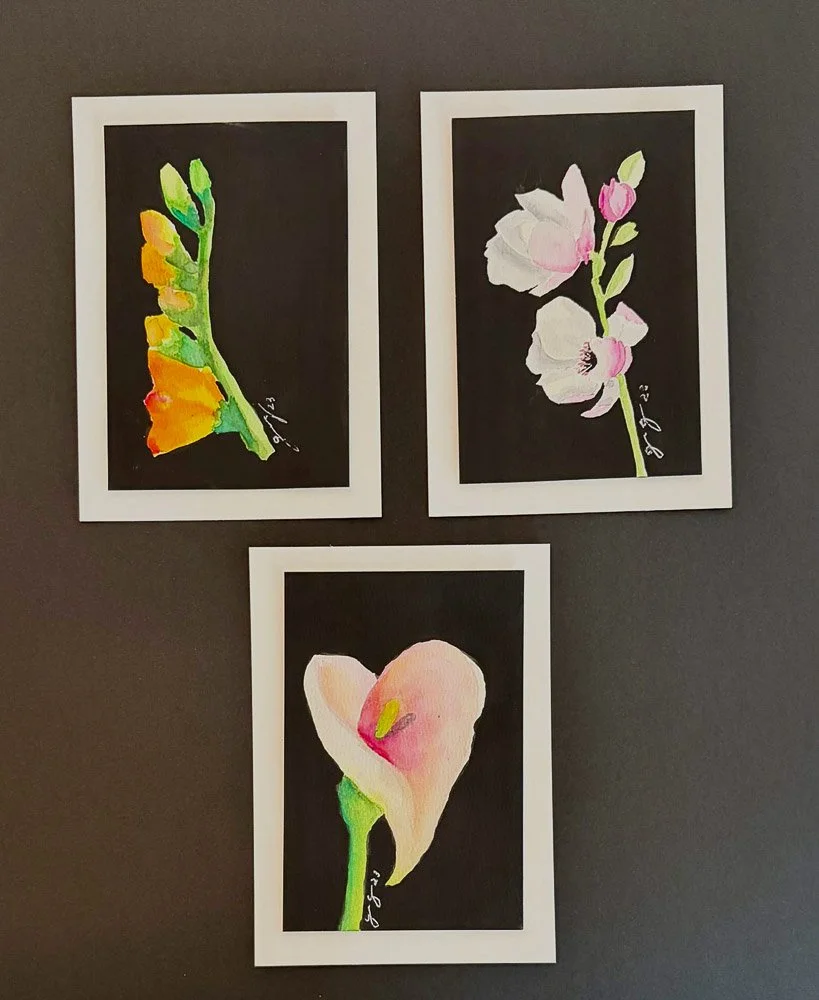 Three watercolor botanical illustrations, each framed in white, featuring a Ginkgo leaf, a cherry blossom, and a calla lily, displayed against a dark background.