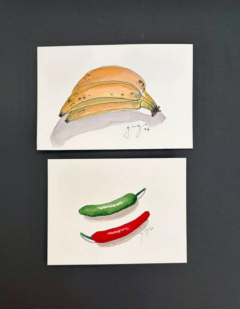 Two watercolor paintings on white paper, one of a bunch of bananas and the other of a green cucumber and a red chili pepper.