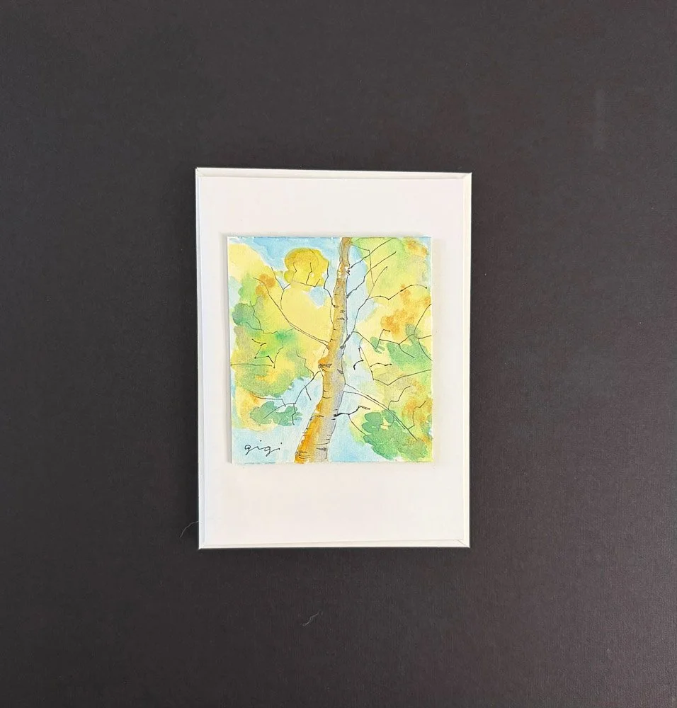 Watercolor painting of a tree with green and yellow leaves, seen from below against a blue sky, framed with a white border.