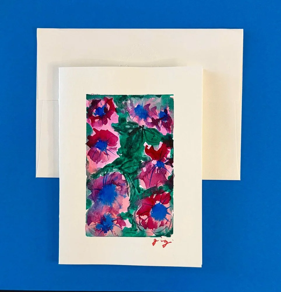 A colorful watercolor painting of pink, red, and purple flowers with green leaves, on white paper, placed on a blue background.