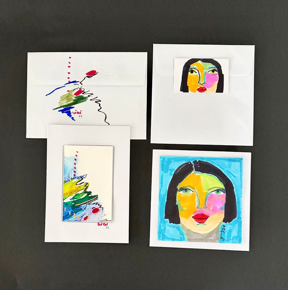 Set of four pieces of artwork and related items including two colorful, stylized portrait paintings of a woman's face, one smaller print of an abstract colorful design, and two white envelopes, one with a smaller version of the abstract design and th