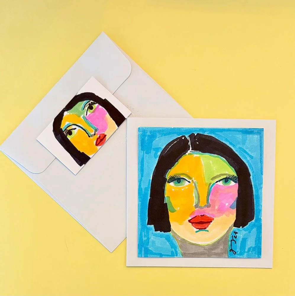Colorful abstract portrait of a woman with black hair, green eyes, yellow and pink face, red lips, and a blue background, along with a smaller version of the same portrait in an envelope.