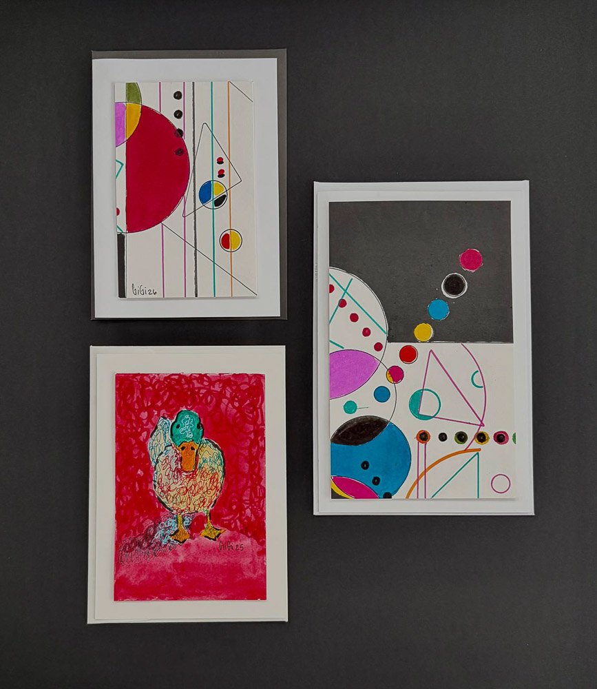 Three framed art pieces on a dark wall: two featuring abstract geometric designs with circles and lines, and one depicting a colorful, scribbled drawing of a dog.