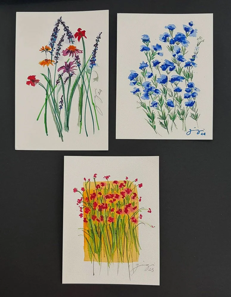 Three watercolor paintings of flowers on white paper: top left shows multicolored flowers including orange, purple, red, and pink with green stems; top right depicts blue flowers with green leaves; bottom features yellow flowers with red blooms and g