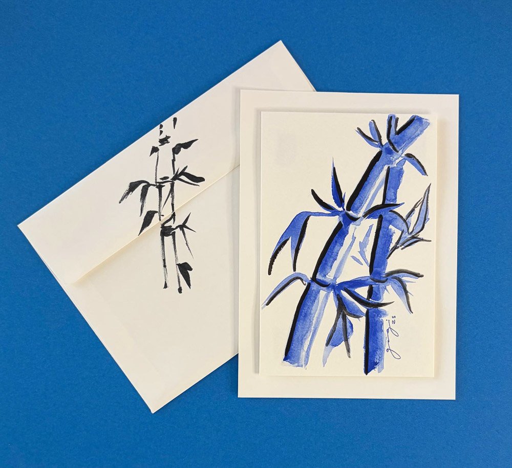 Art prints of bamboo stalks and leaves, one in black ink and one in blue watercolor, placed on blue background with matching envelope.