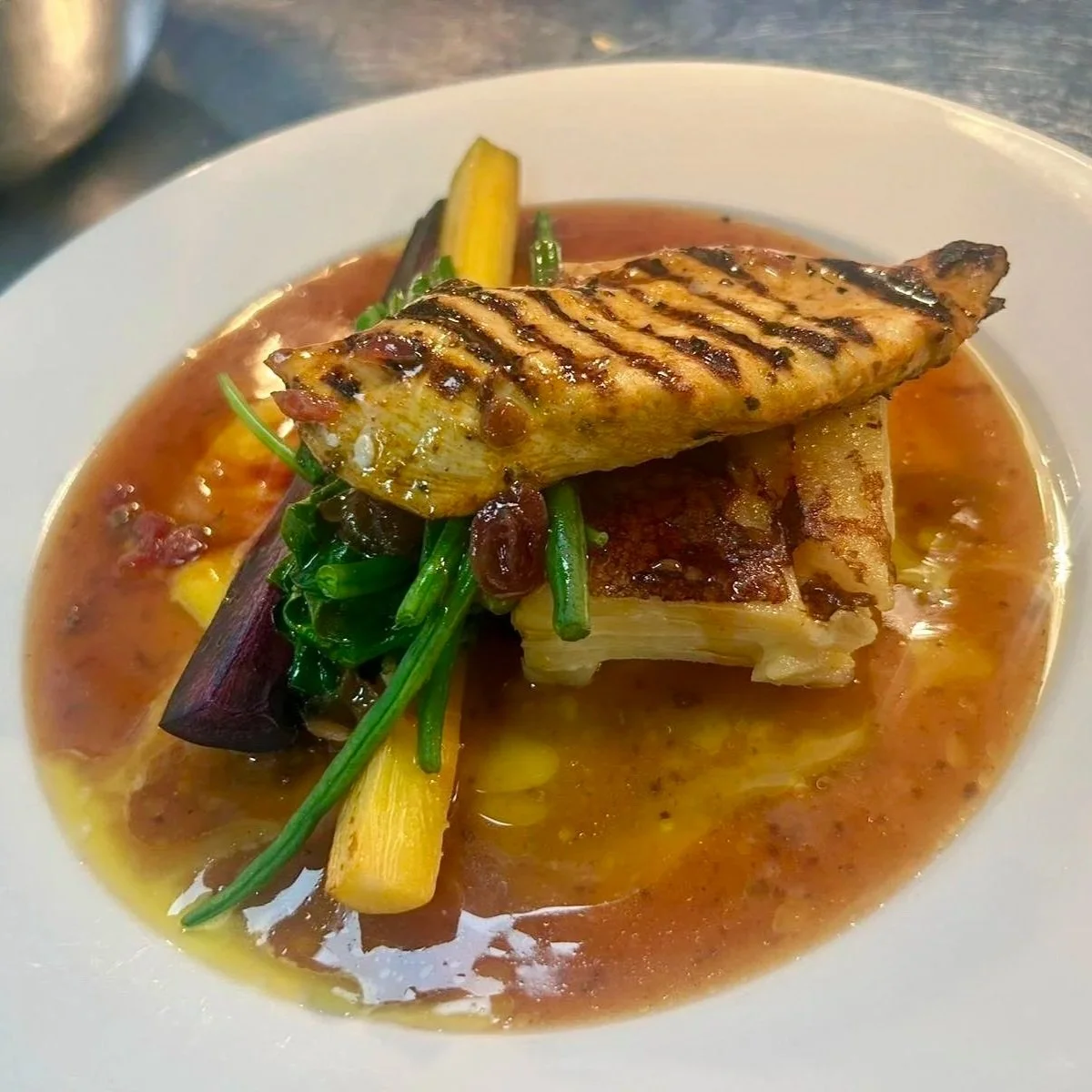 Grilled fish fillet with vegetables and sauce on a white plate.