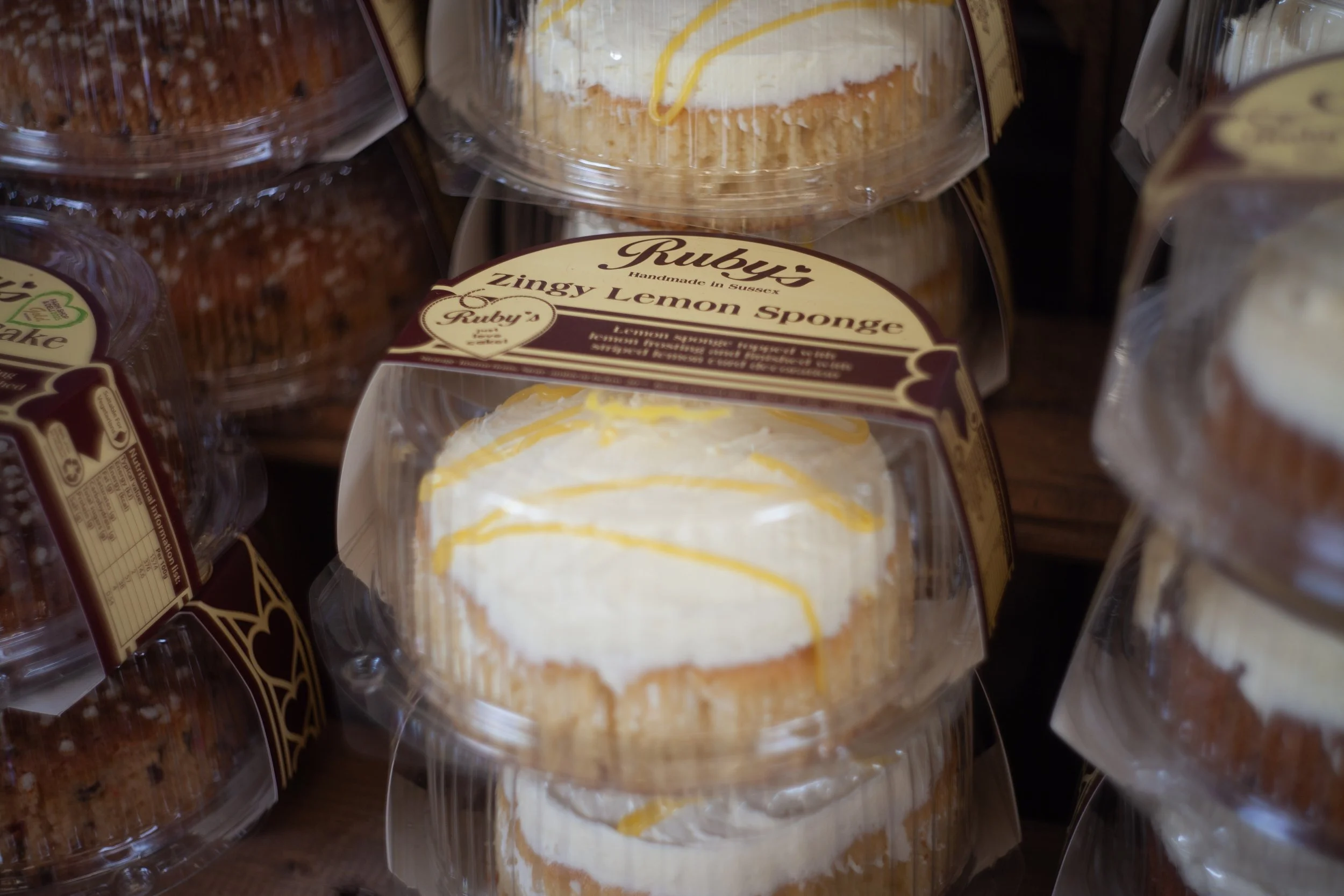 A bakery display case with a variety of cakes, including a lemon sponge cake with lemon topping from Ruby's.