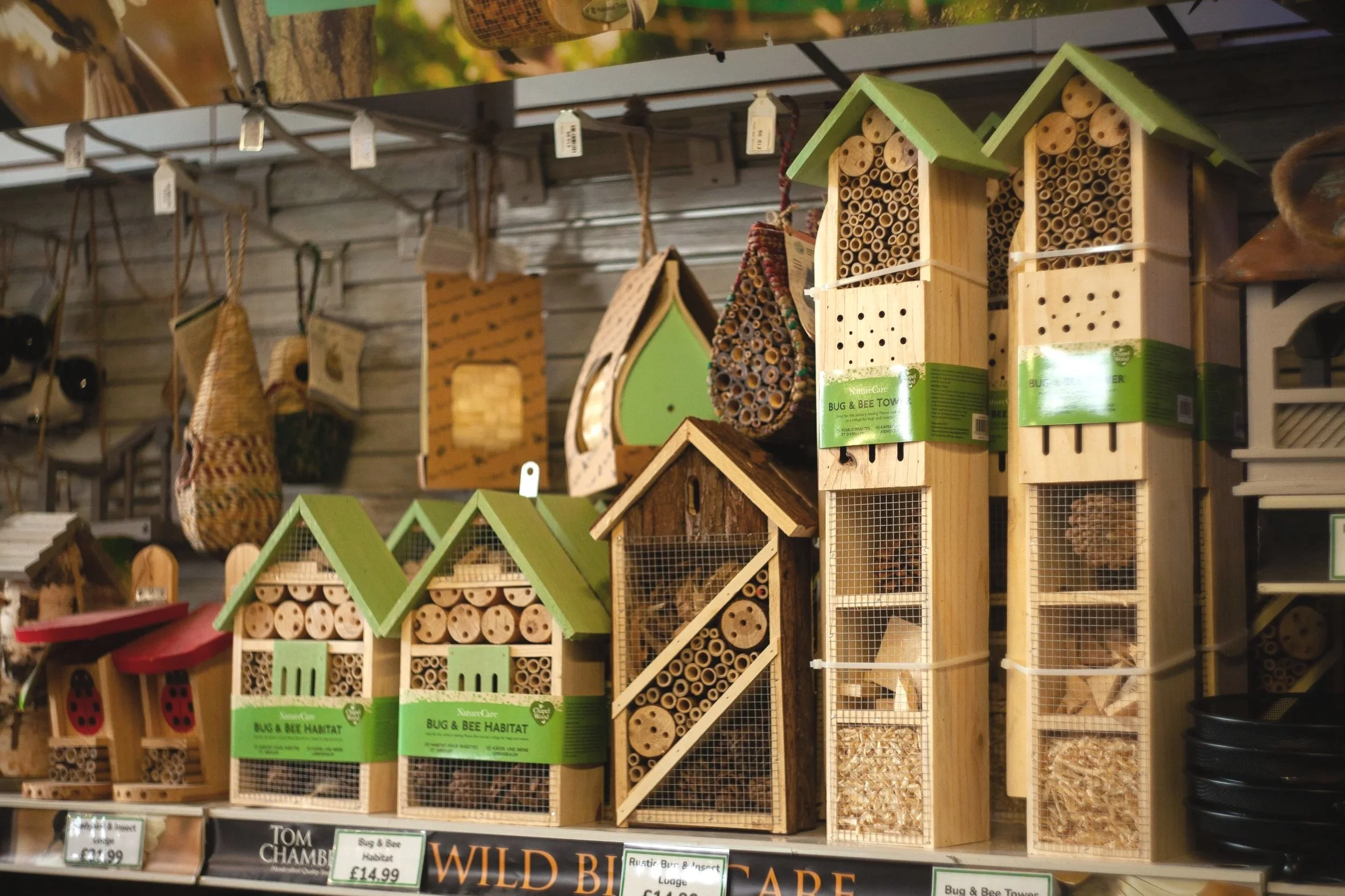 Various wooden and plastic insect hotels with straw, bamboo, and wood materials on display in a store.