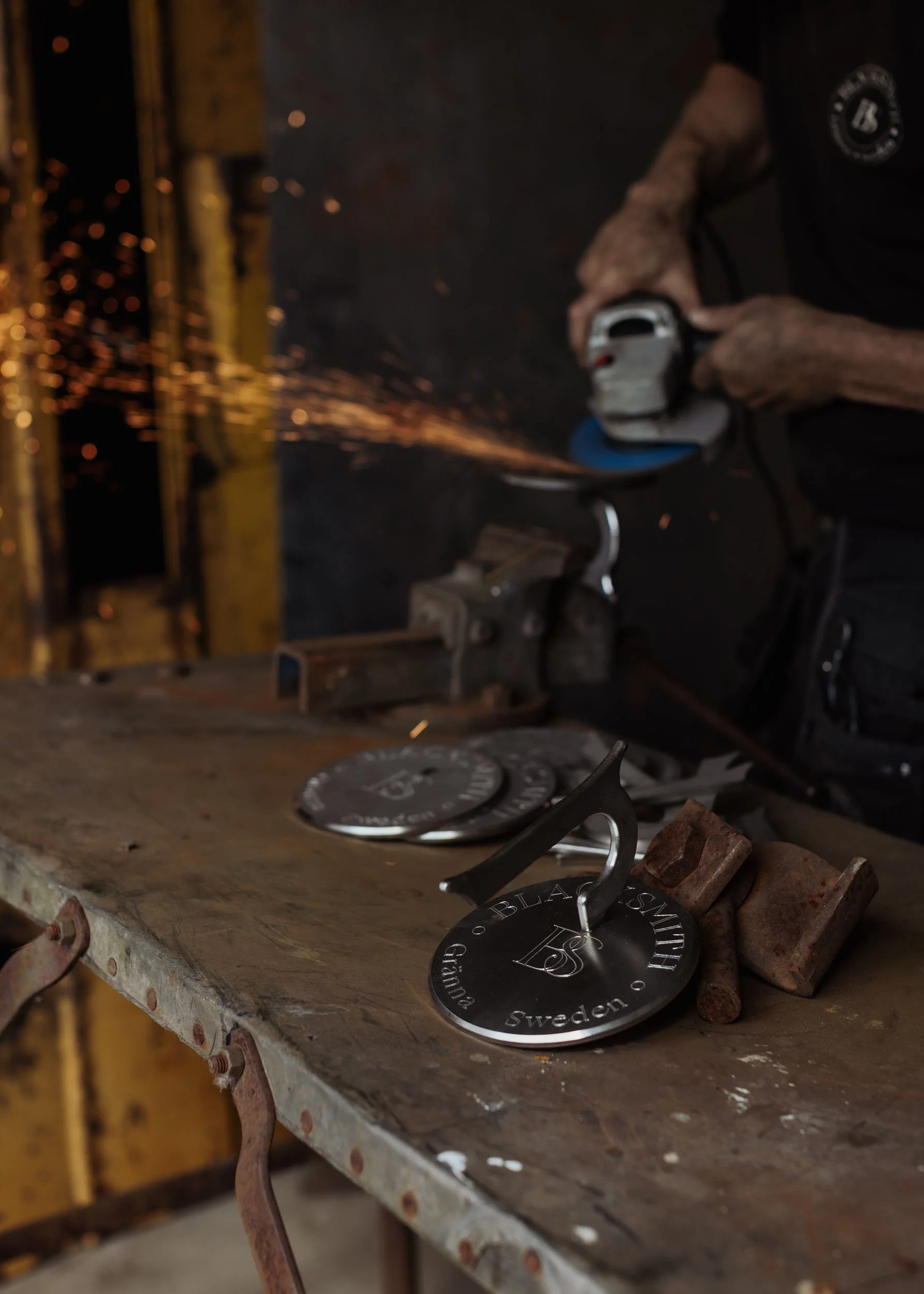 En person slipar en rund metallen detalj med en slipmaskin, varav delar av detaljen har texten 'Gothenburg Sweden' och 'Blacksmith 182'.