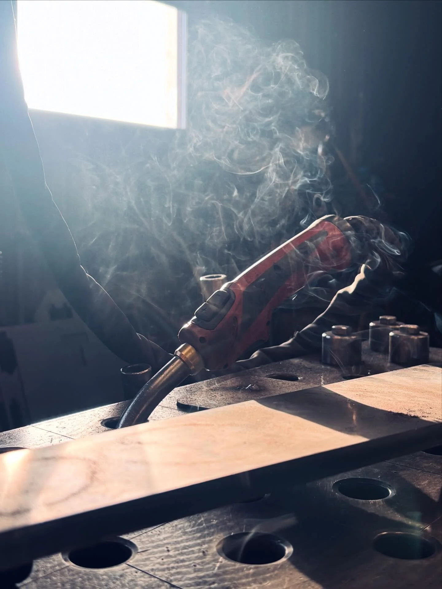 En person använder en svetsmaskin för att svetsa på ett metallbord, vilket orsakar rök och ljus.