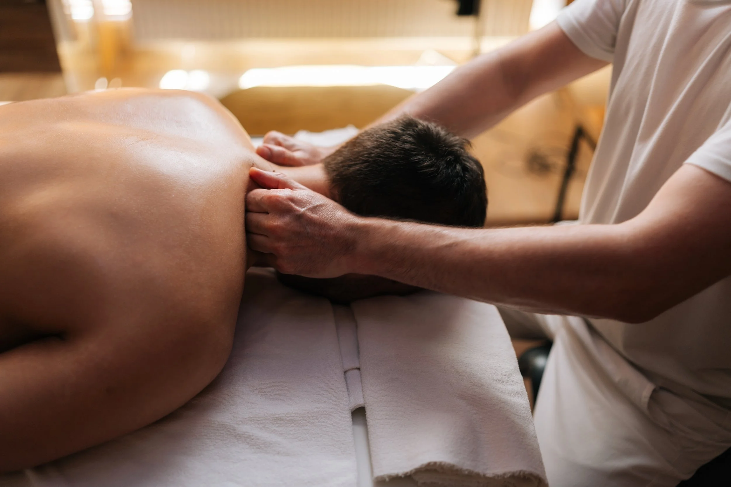 Eine Person liegt auf einem Massagetisch und wird im Nacken massiert.