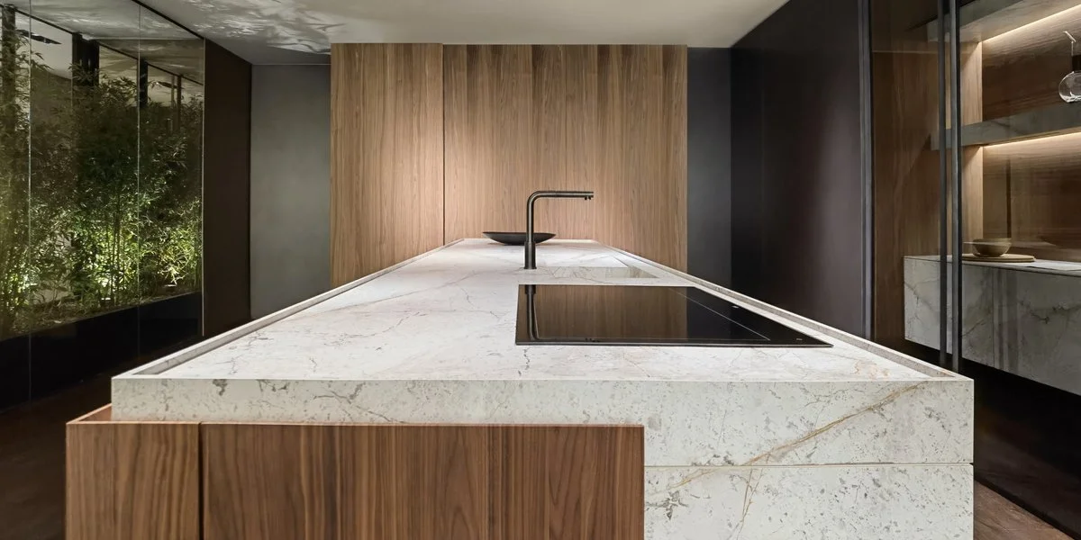 Cucina moderna con isola in marmo bianco con venature, ambiente elegante con pareti in legno e mobili in marmo e legno.