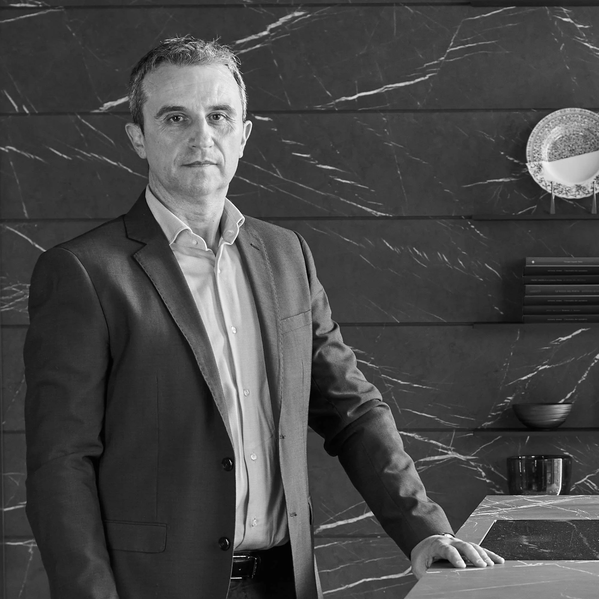 Uomo d'affari in giacca formale si appoggia su un tavolo in un ambiente elegante con pareti di marmo scuro e decorazioni sofisticate.